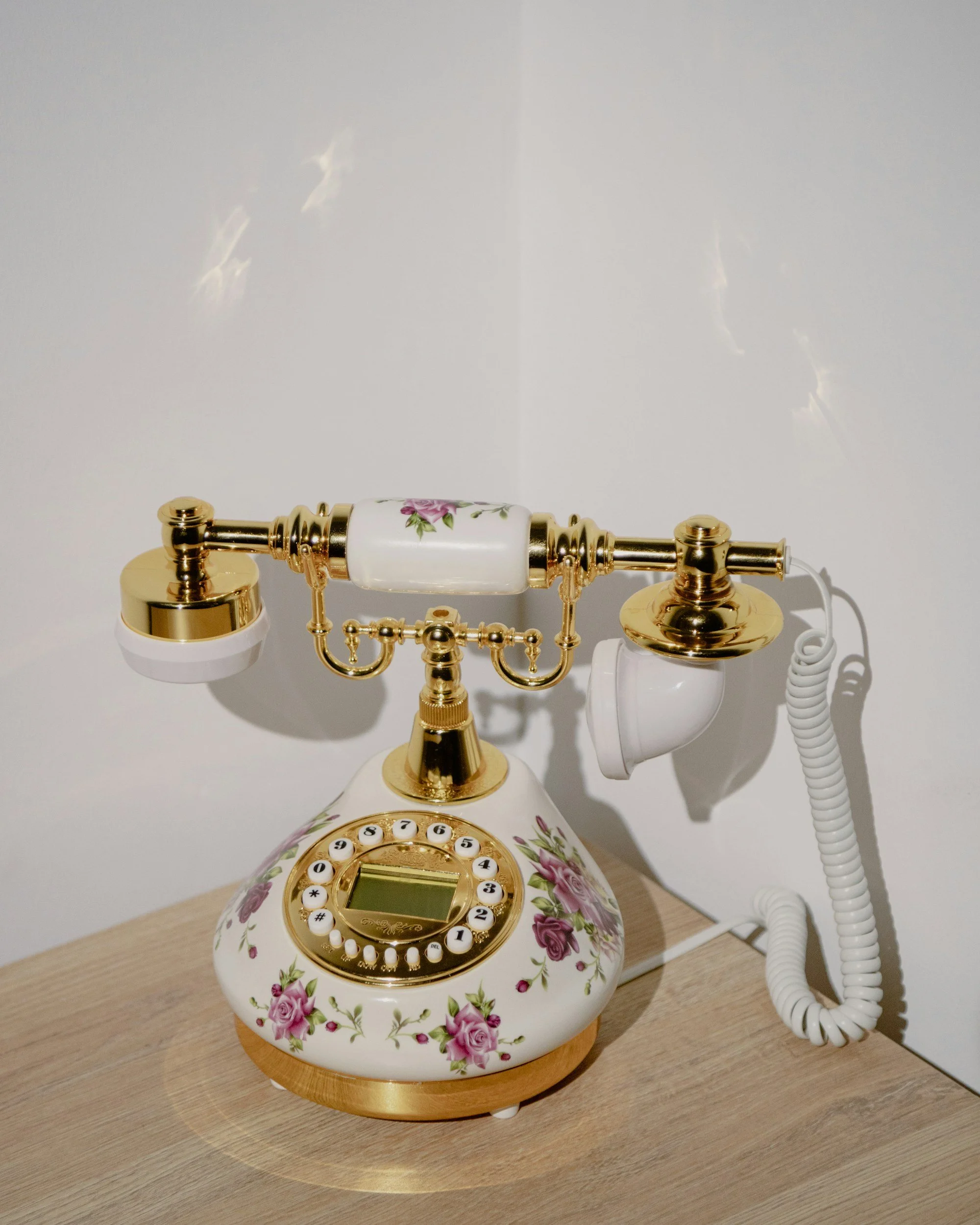 Decorative vintage rotary phone with floral patterns on a wooden surface.
