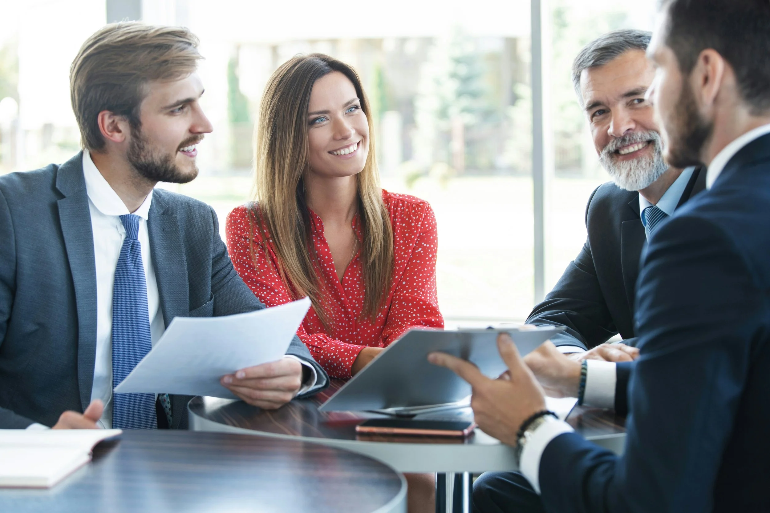 Group of five professionally dressed people having a business meeting or discussion around a table in a bright office setting