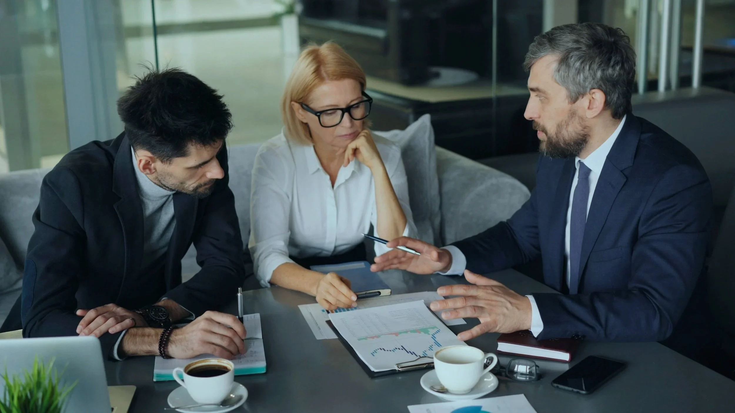 Three professionals engaged in a serious business discussion at a conference table in a modern office.