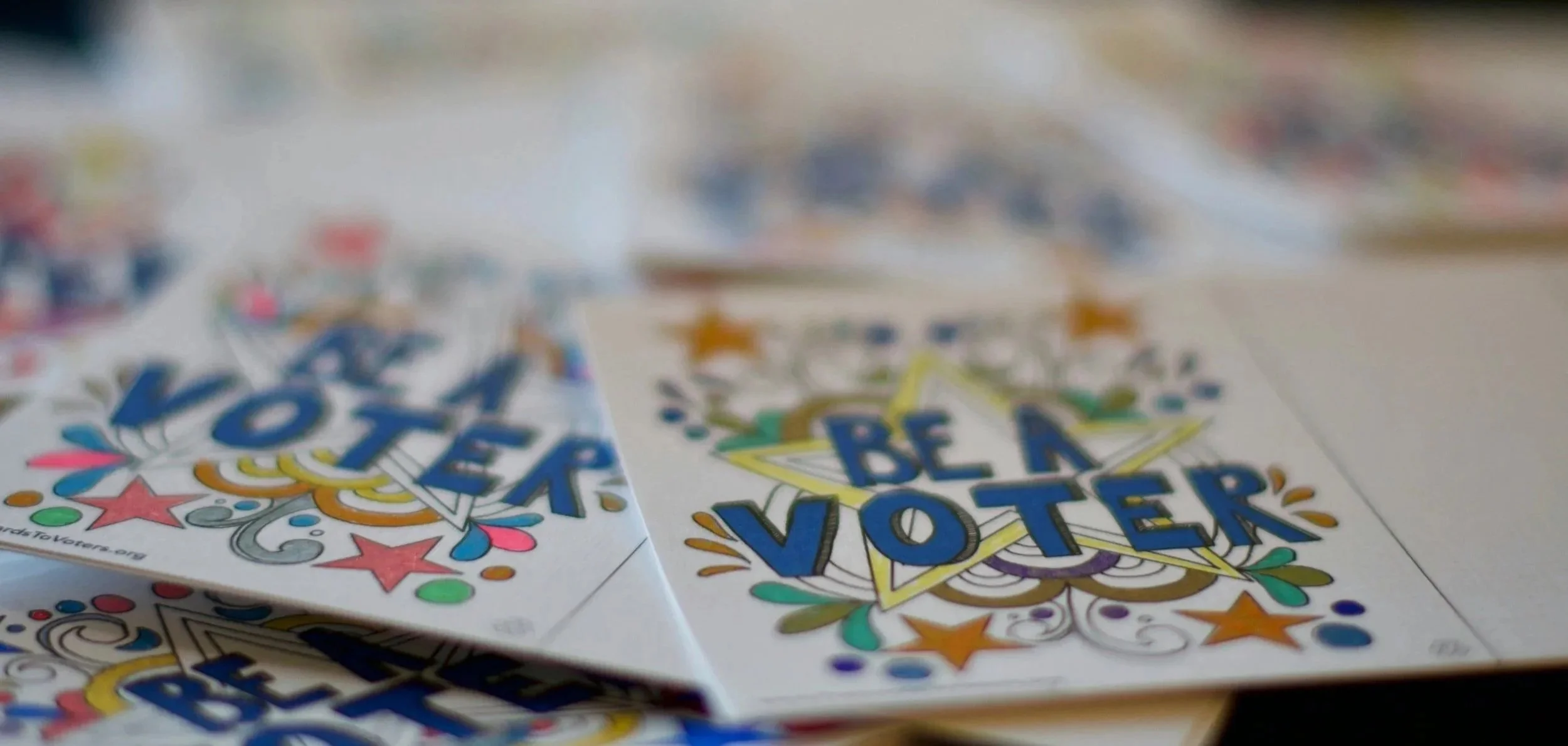 Colorful election campaign flyers with the phrase "BE A VOTER" on a table.