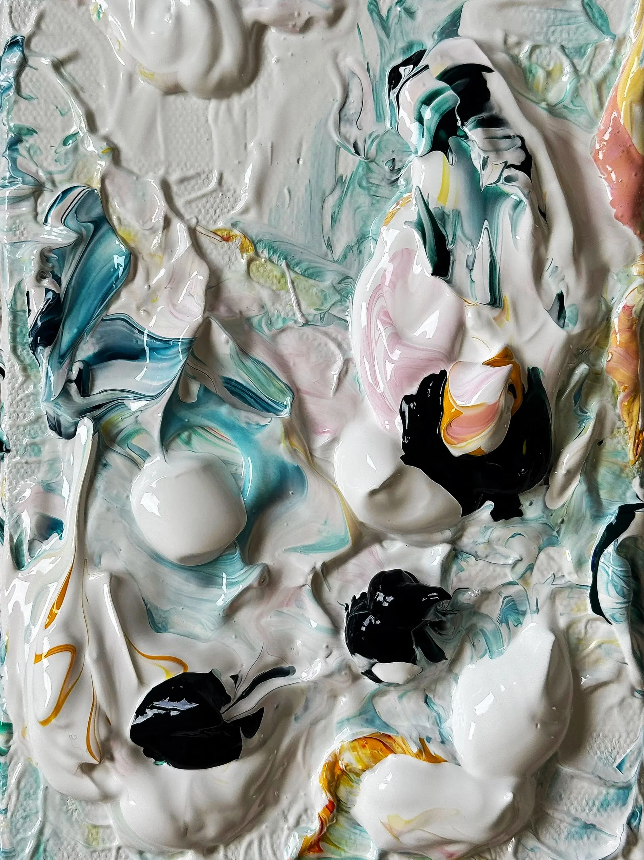 Close-up of a mixture of various paint colors swirled and blended together in an abstract pattern, including white, black, blue, pink, yellow, and green.