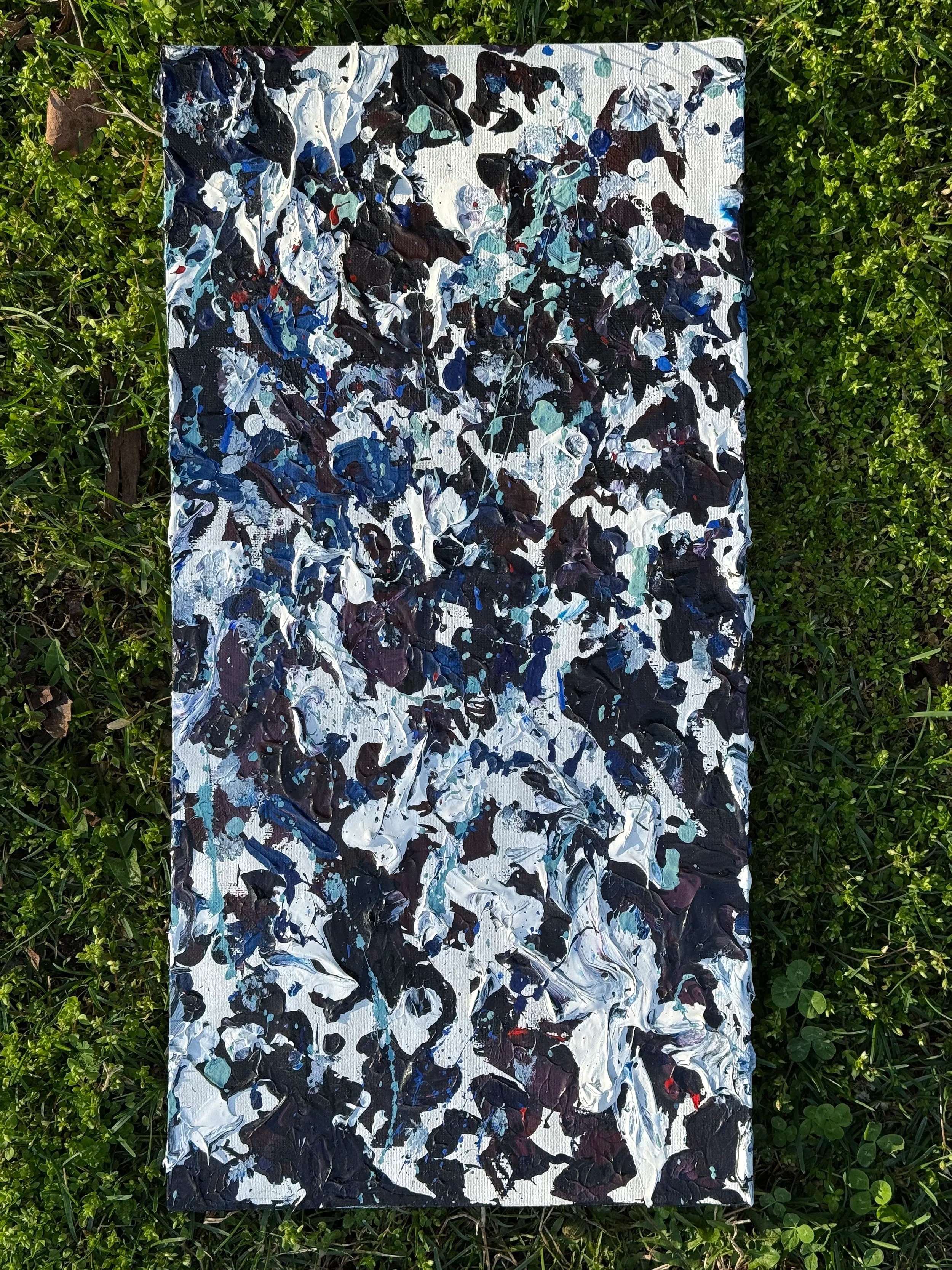 Abstract expressionist painting with bold splashes and strokes of black, white, blue, and hints of teal and red on a canvas placed on green grass.