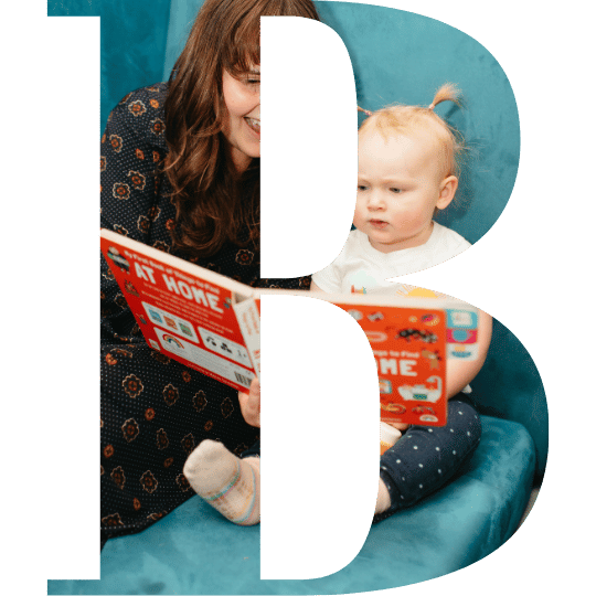 A woman and a young girl sitting on a blue couch, reading a book together.
