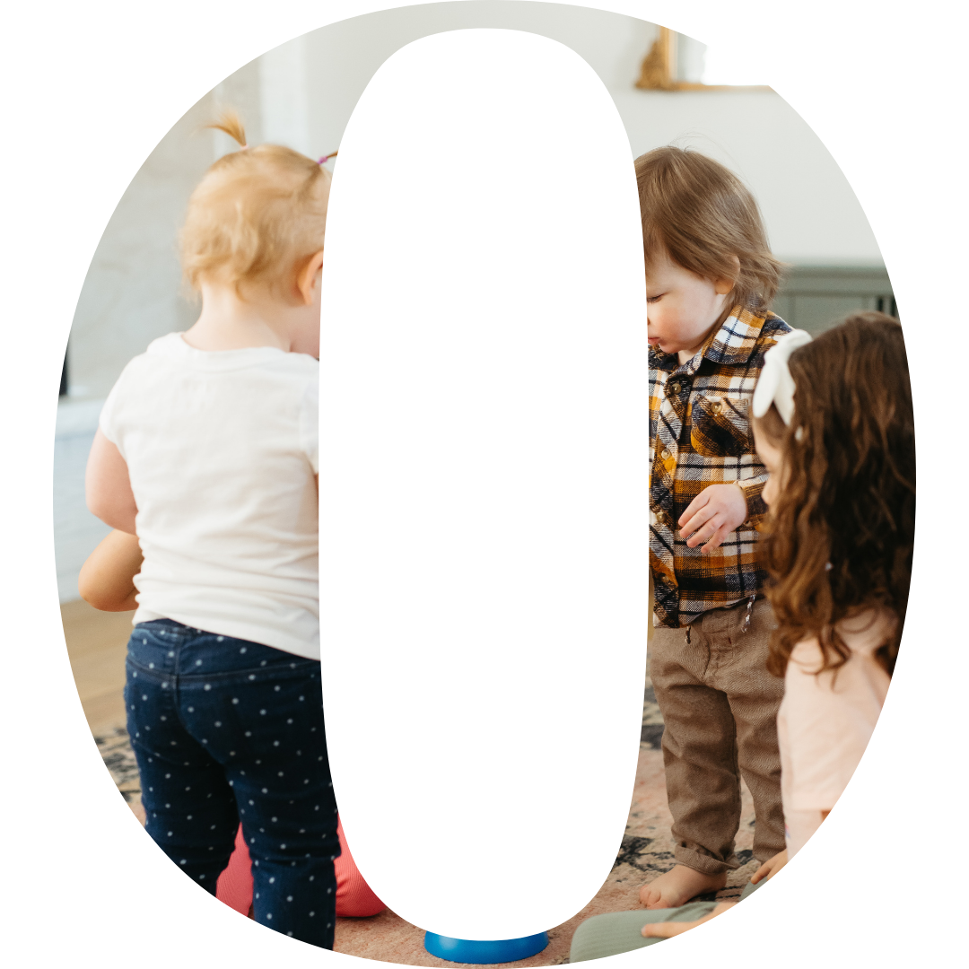 Three young children playing with a bubble machine indoors.
