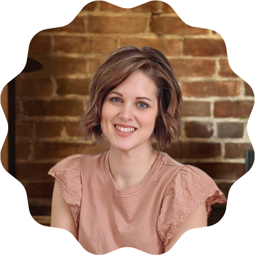 A woman (Madison Hughes) with short brown hair smiling, wearing a light pink top with ruffled sleeves, sitting in front of a brick wall.