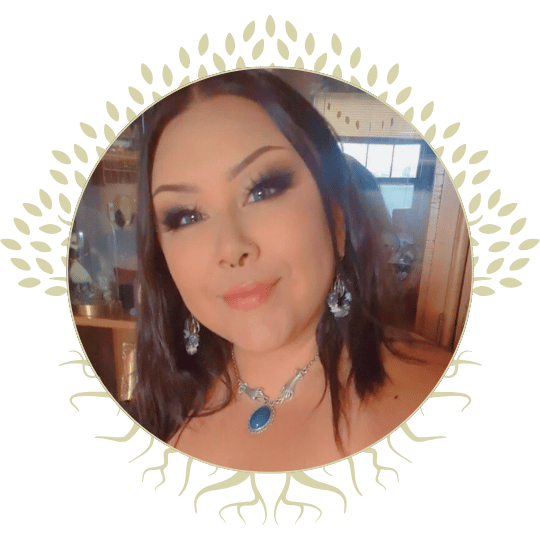 A woman (Alyssa Guimond) with dark hair, wearing jewelry including earrings and a necklace with a blue gemstone, posing indoors with a confident expression.