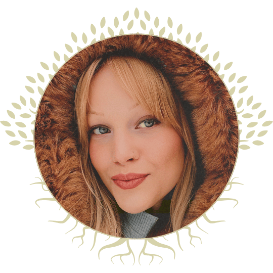 A woman (Piper Rasmussen) with blonde hair, blue eyes, and a nose piercing, wearing a hooded jacket with faux fur trim, surrounded by a decorative circular tree pattern.