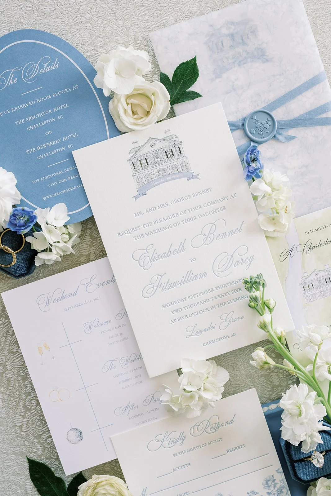 Blue and white, elegant wedding stationery suite surrounded by real flowers with blue wax seals and other wedding details on a neutral background

