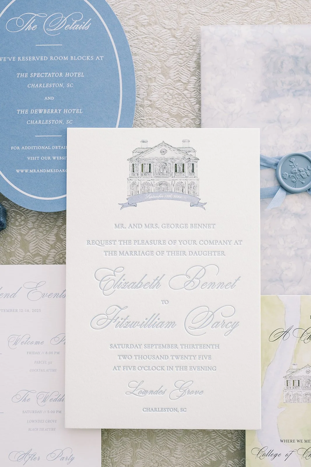 Blue and white wedding invitation with stationery details behind it featuring hand-drawn venue illustration