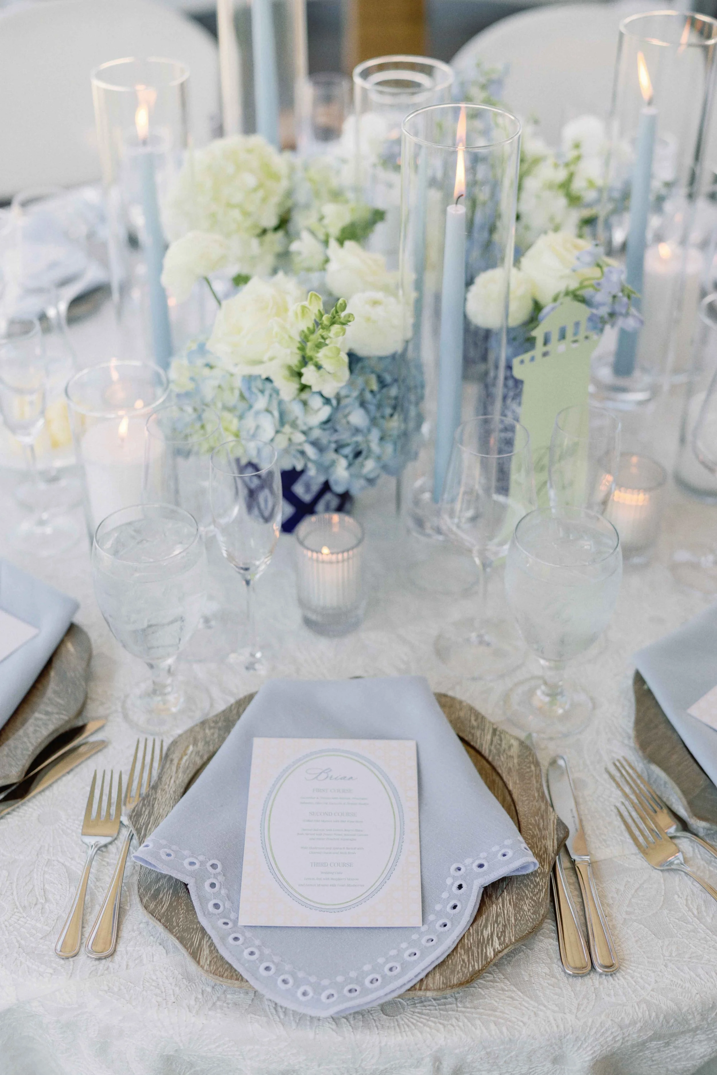 Elegant reception table set-up with blue and white florals, custom menus, candles, and various dinnerware