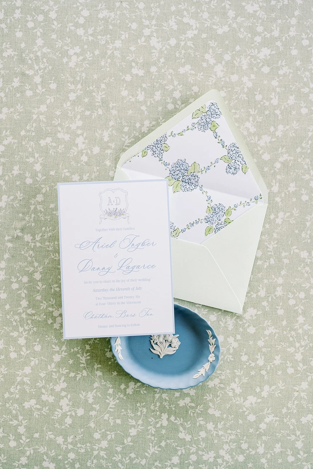 Wedding invitation with a custom wedding envelope liner and a green envelope next to a blue ring dish on a green background