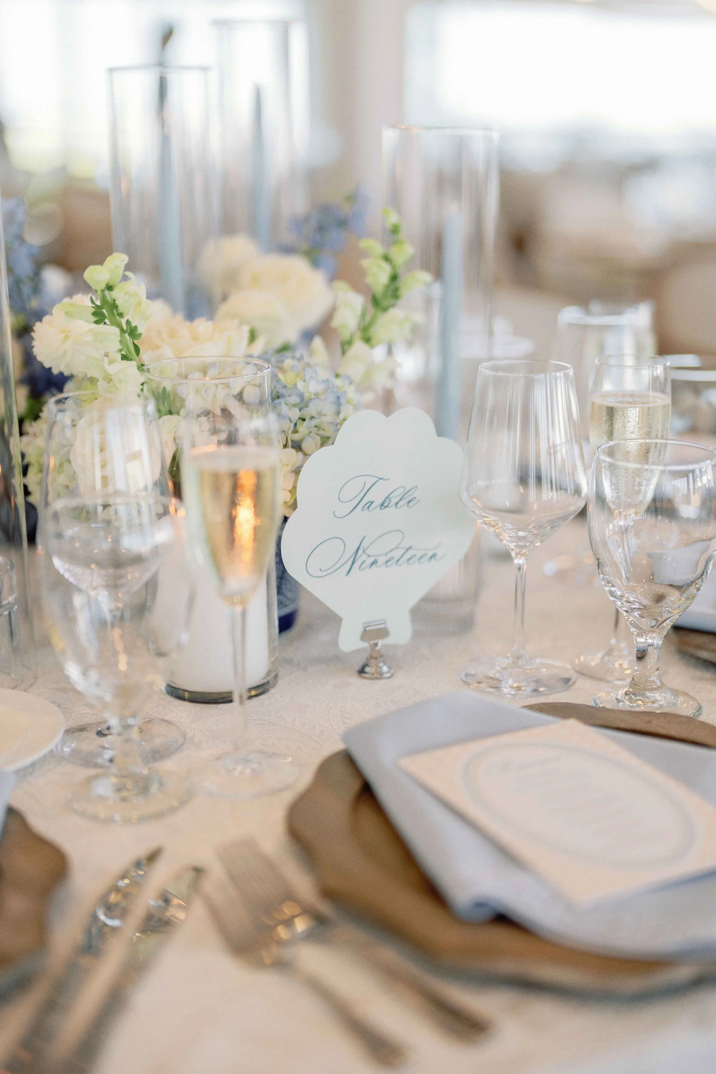 A shell-shaped table number sitting on a reception table surrounded by flowers and dinnerware.