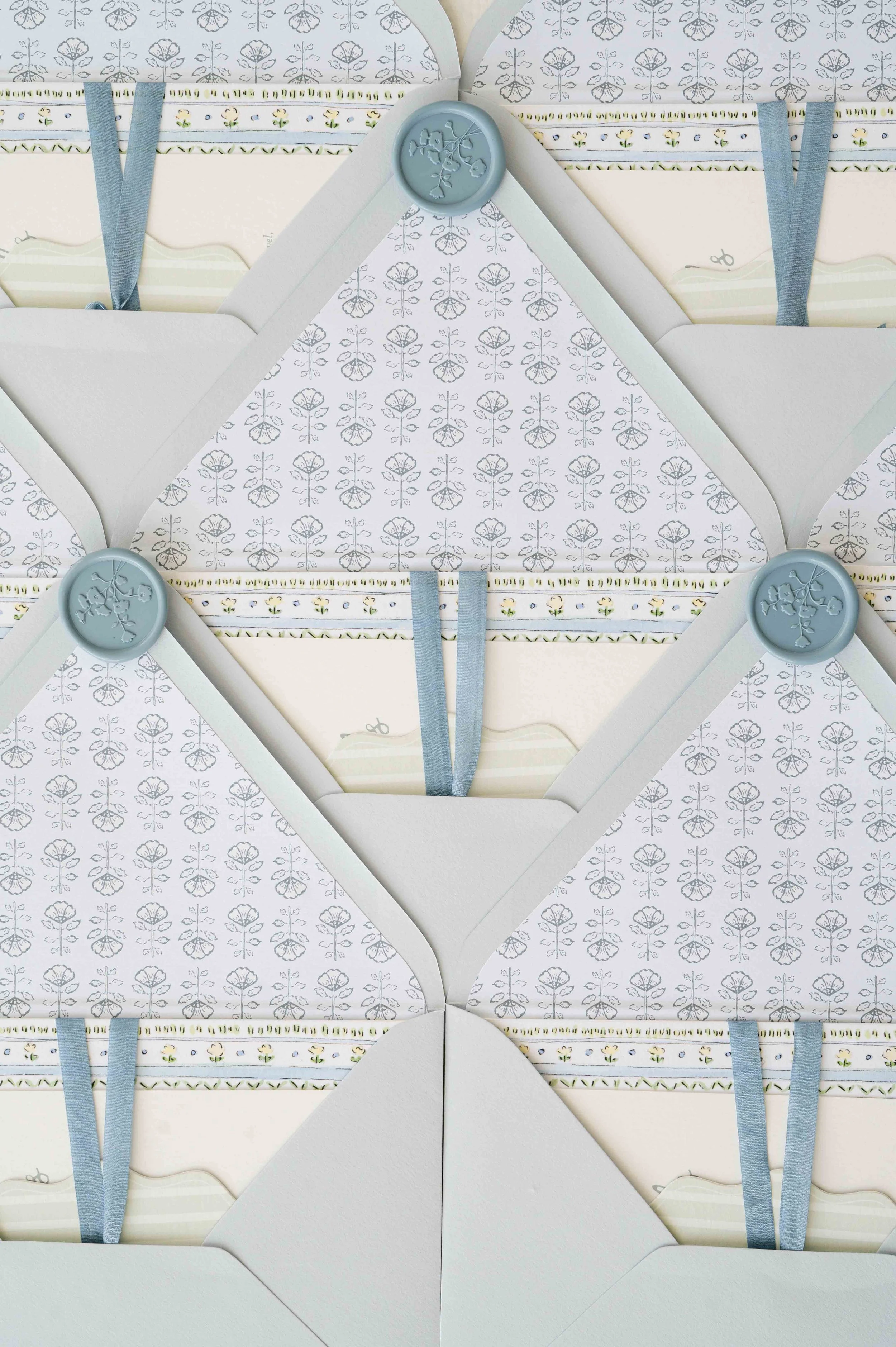 Multiple envelopes with envelope liners, secured with blue wax seals with floral designs, and blue ribbons, arranged in a pattern.