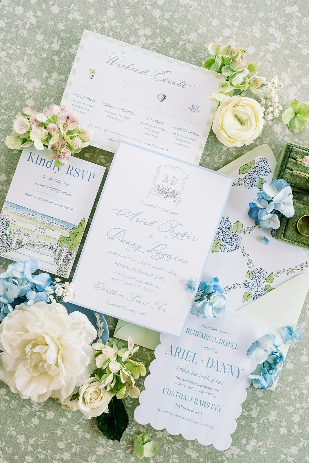 Wedding invitation suite with floral accents including roses and hydrangeas on a green tablecloth.