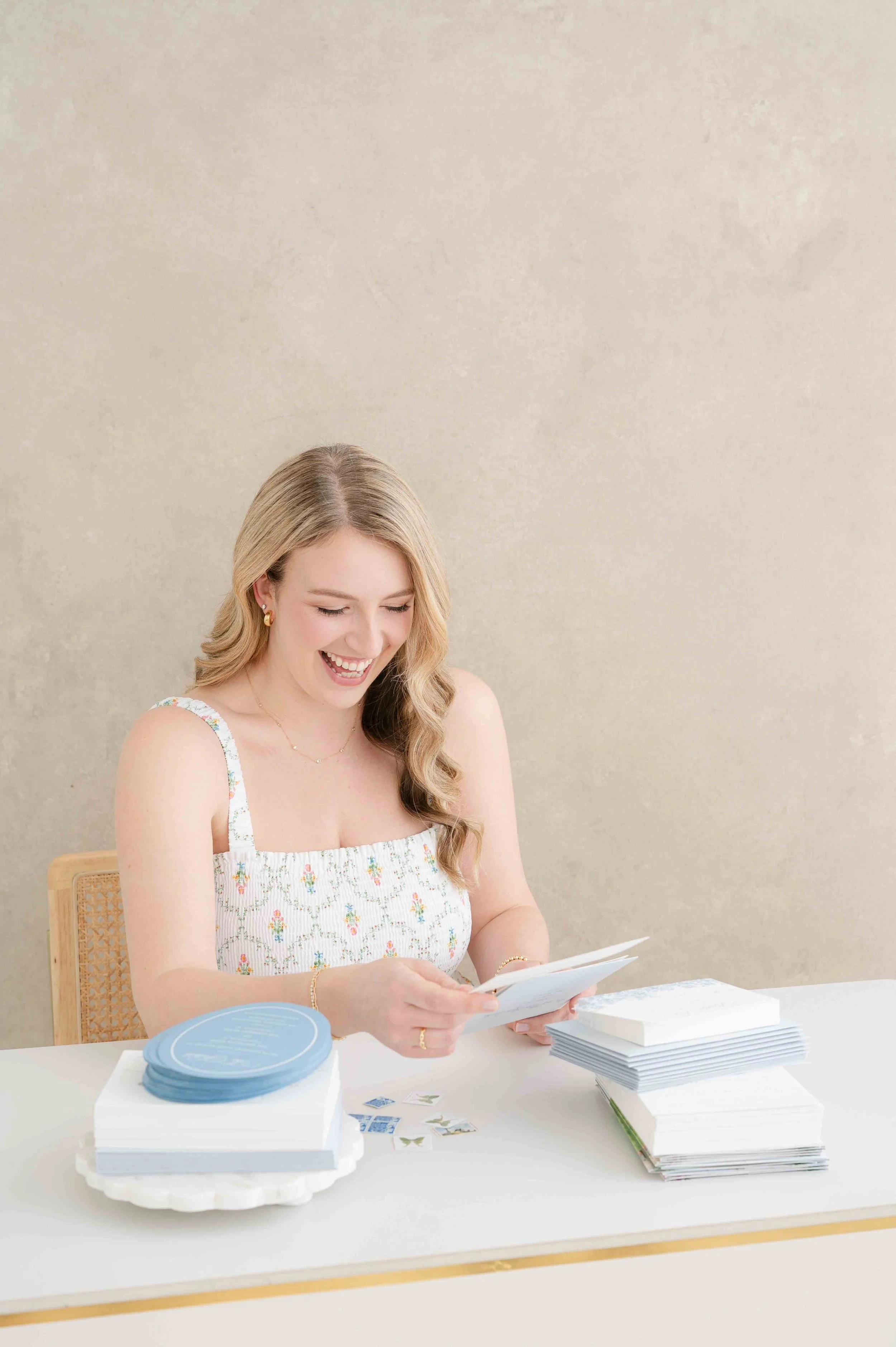 A woman with blonde hair smiling and looking down at a wedding invitation while assembling the invitations.