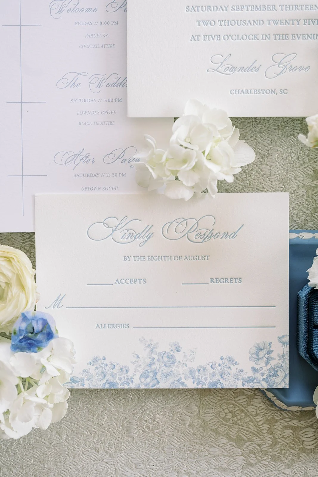 RSVP card with blue floral details on the card surrounded by real flowers on a neutral background