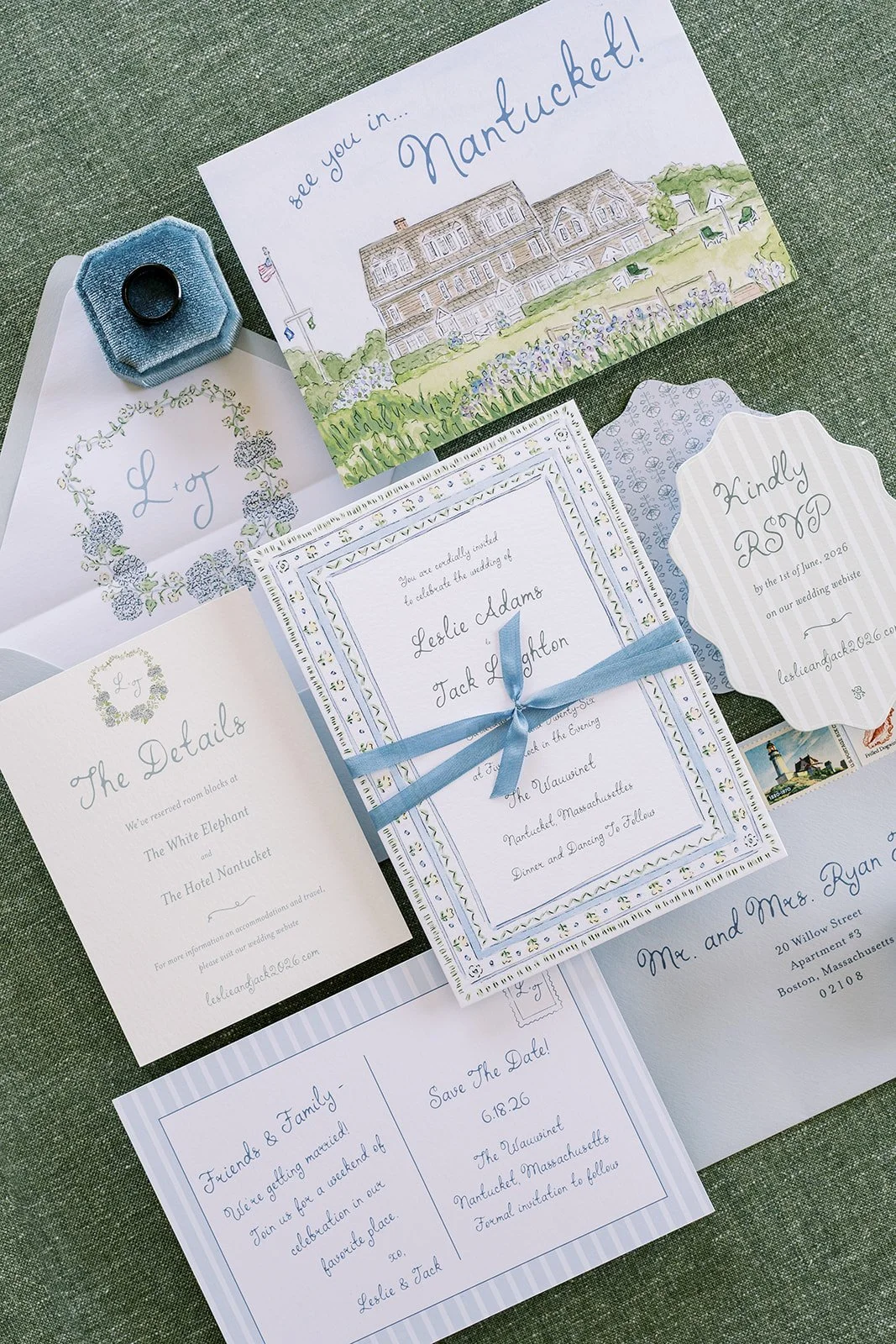 Wedding invitation suite including a main invitation with a blue ribbon, RSVP card, details card, and a Nantucket-themed save the date, all placed on a green surface.