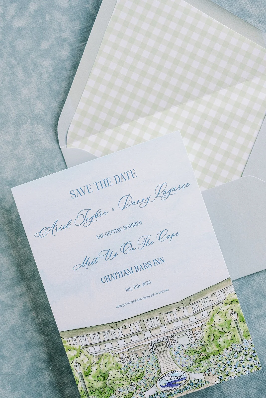 Custom watercolor artwork on a save the date card next to a blue envelope with a custom gingham liner on a blue background