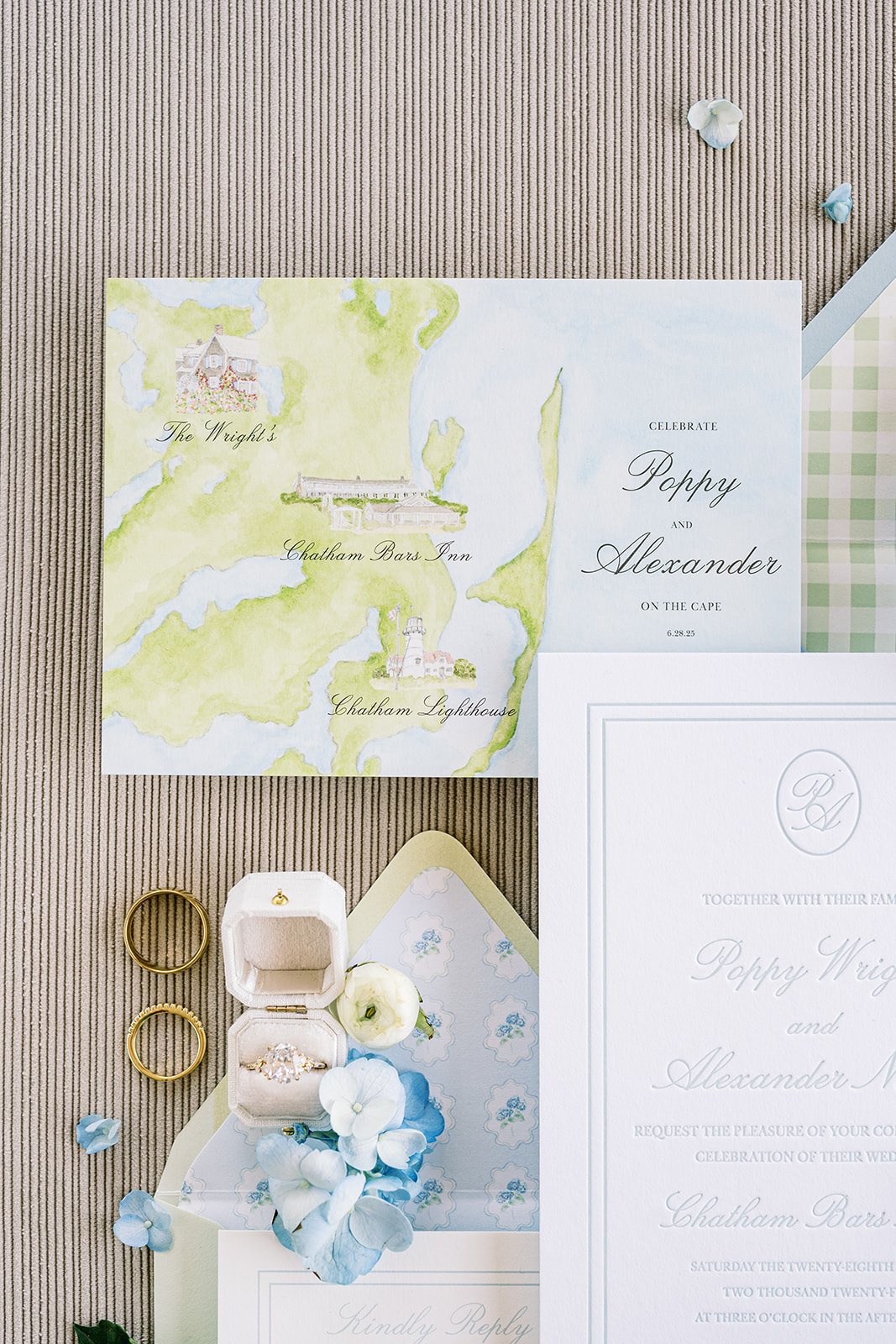 Custom watercolor wedding invitation map next to wedding stationery, rings, and real florals on a neutral background