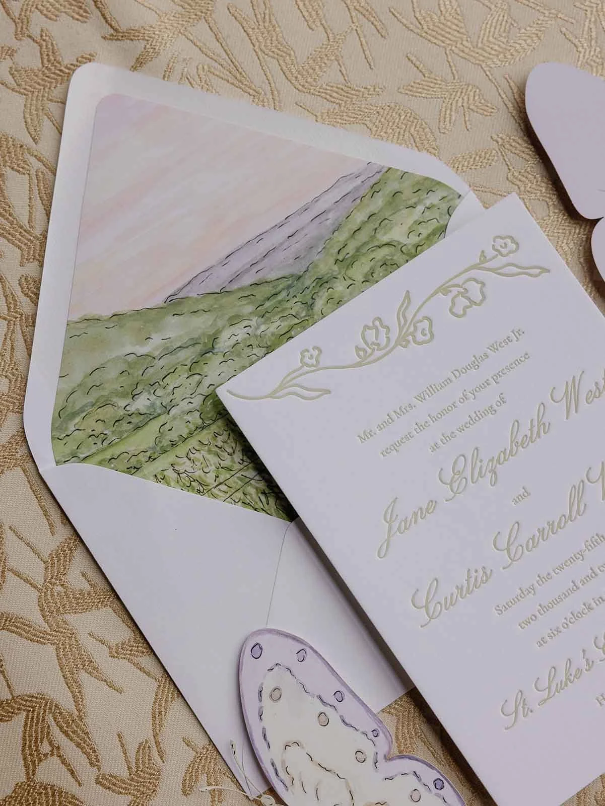 Envelope liner with watercolor artwork and wedding invitation on top of a gold pattern background