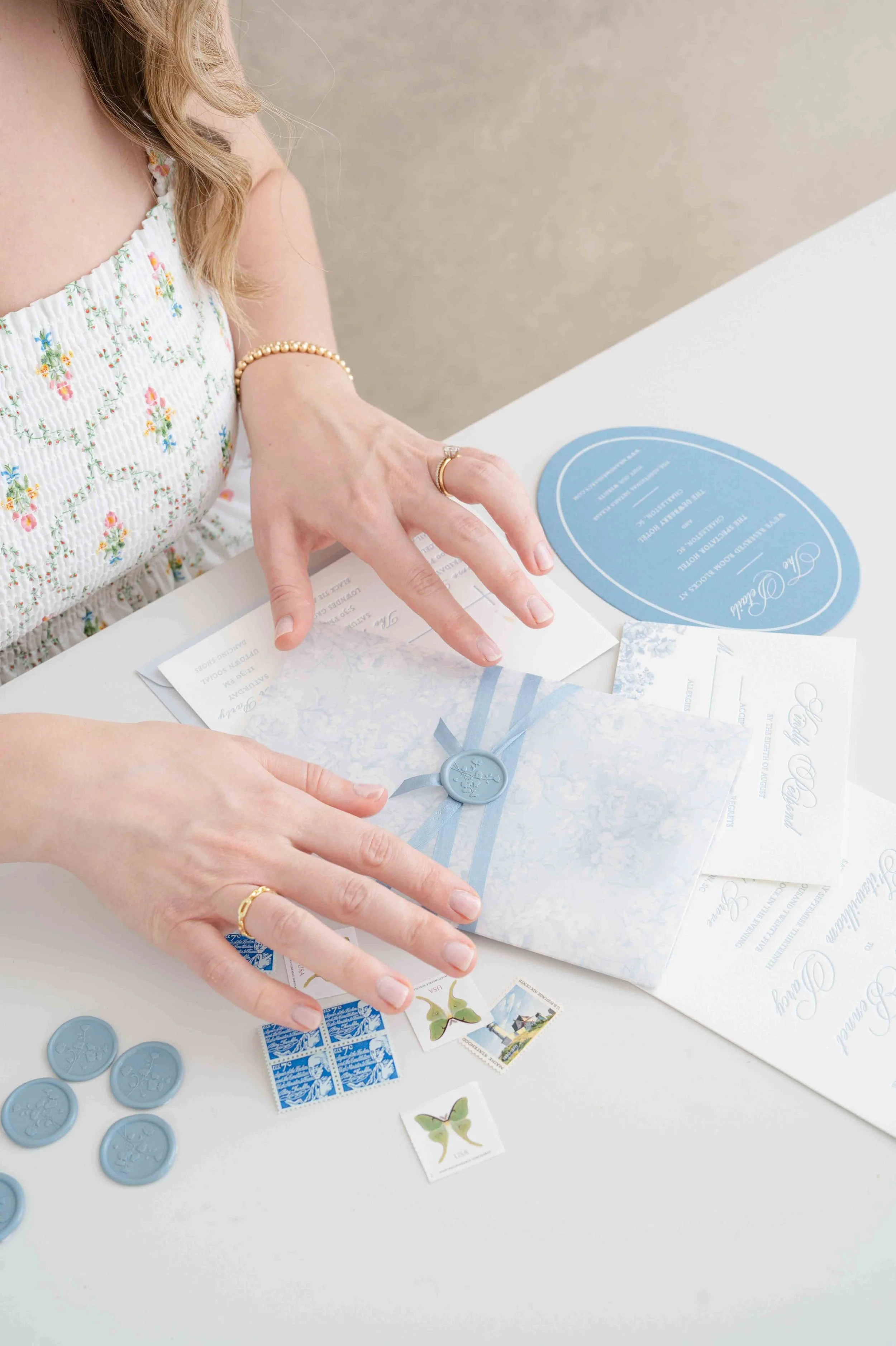 Person preparing wedding invitations with blue envelopes, stamps, and seals on a white table.