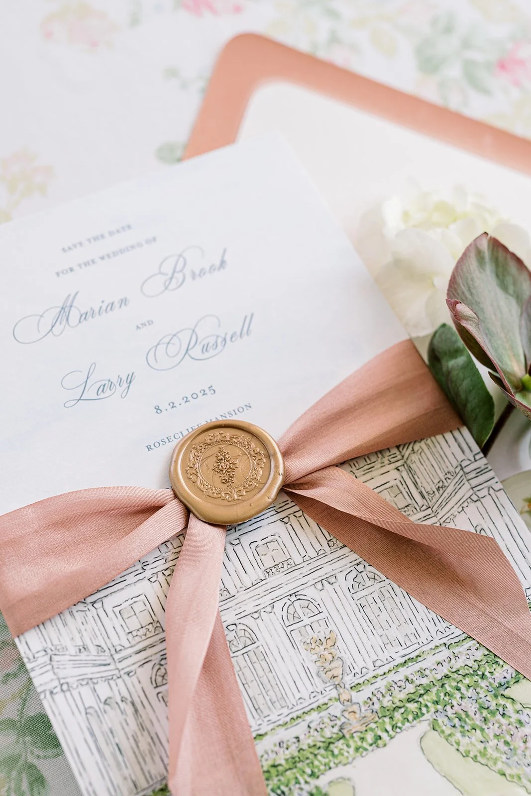 Romantic and pink wedding stationery created by a watercolor artist featuring a custom hand-drawn venue illustration with a pink ribbon, gold wax seal, and pink envelope on a floral background
