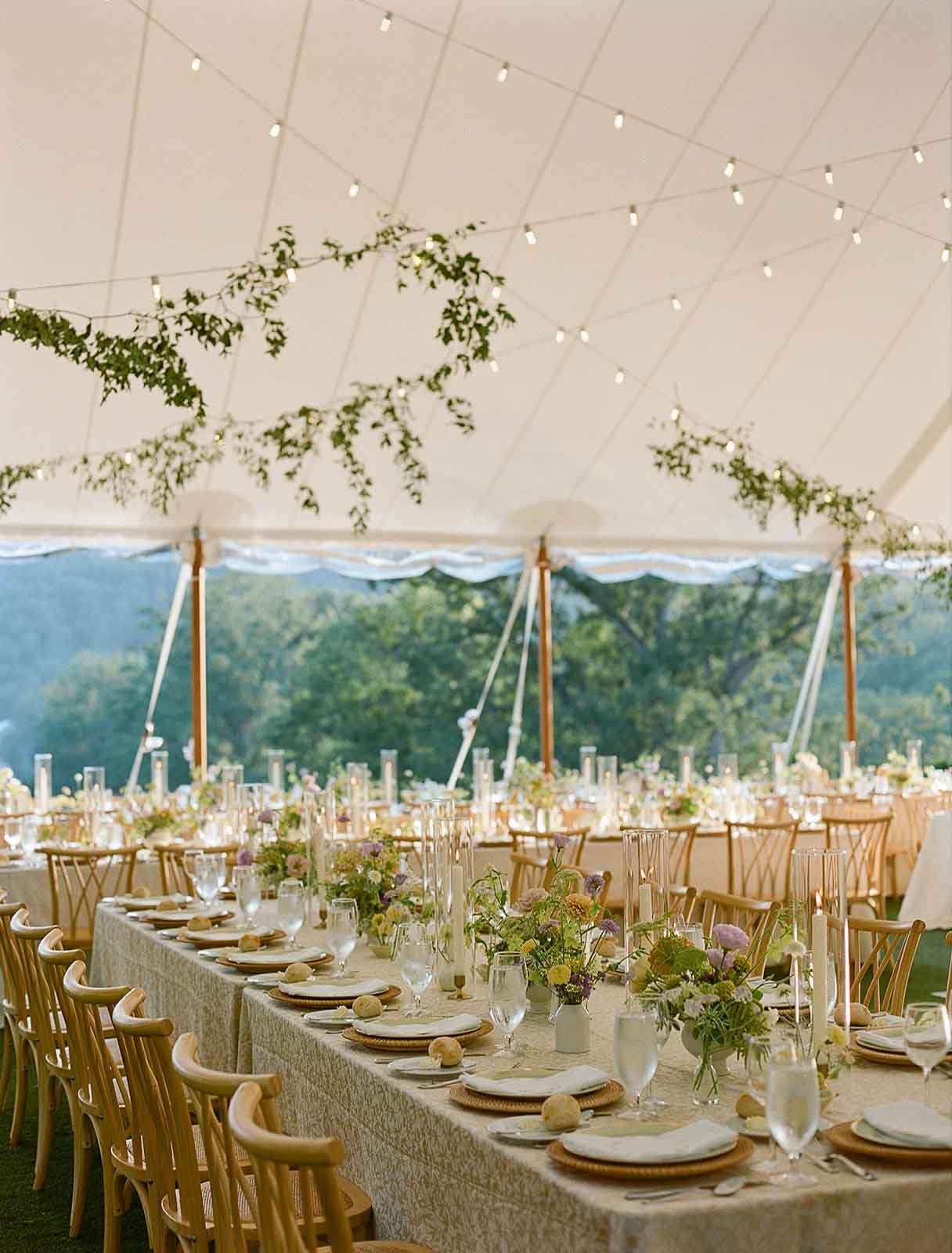 Outdoor tent with string lights and greenery hanging above guest dining tables