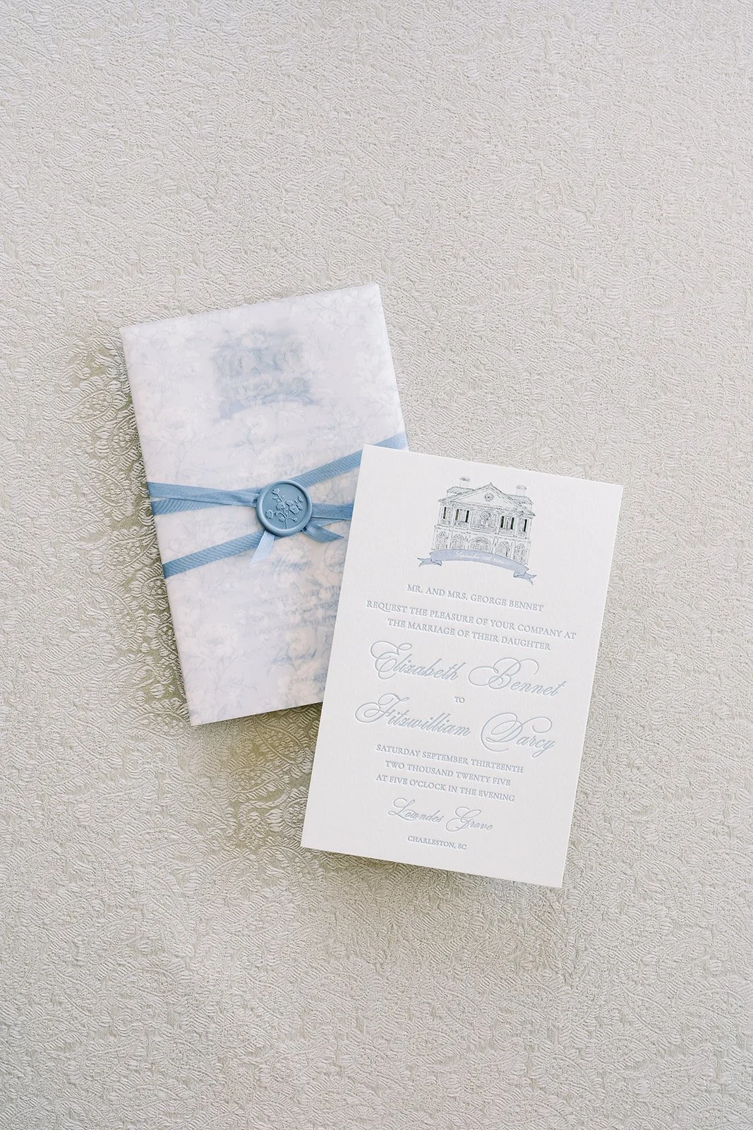 Custom wedding invitations with a blue wax seal and blue ribbon on a neutral background