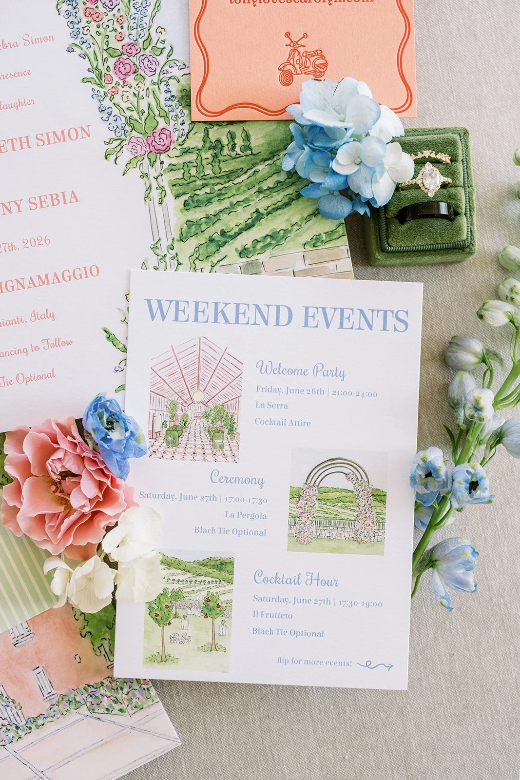 A wedding invitation celebrating weekend events for a destination wedding including a welcome party, ceremony, and cocktail hour, surrounded by flowers with a small vintage watercolor illustration of a landscape and an archway decorated with flowers.
