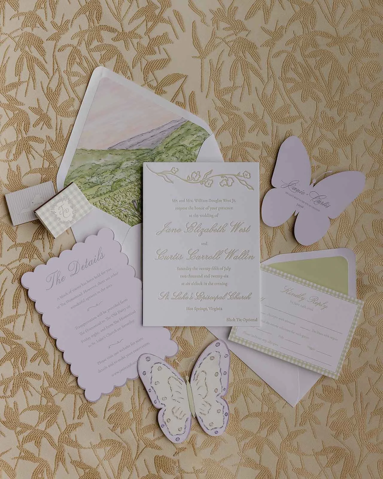 Stationery suite laying on top of a gold background featuring butterfly cut-outs, invitations, watercolor envelope liners, and more for a whimsical wedding stationery design