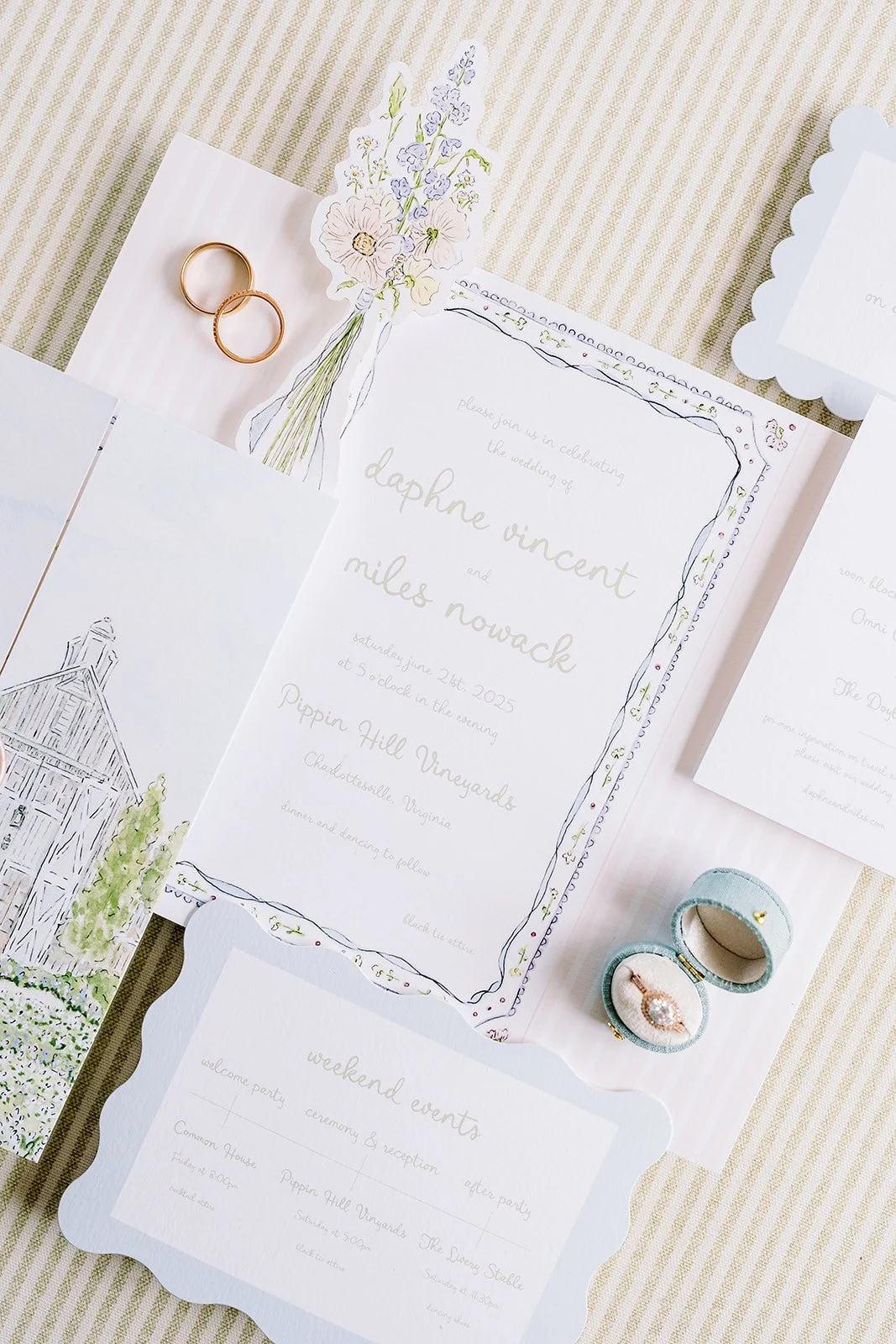 Wedding invitation suite and details for a wildflower-themed wedding surrounded by decorative paper and wedding rings.