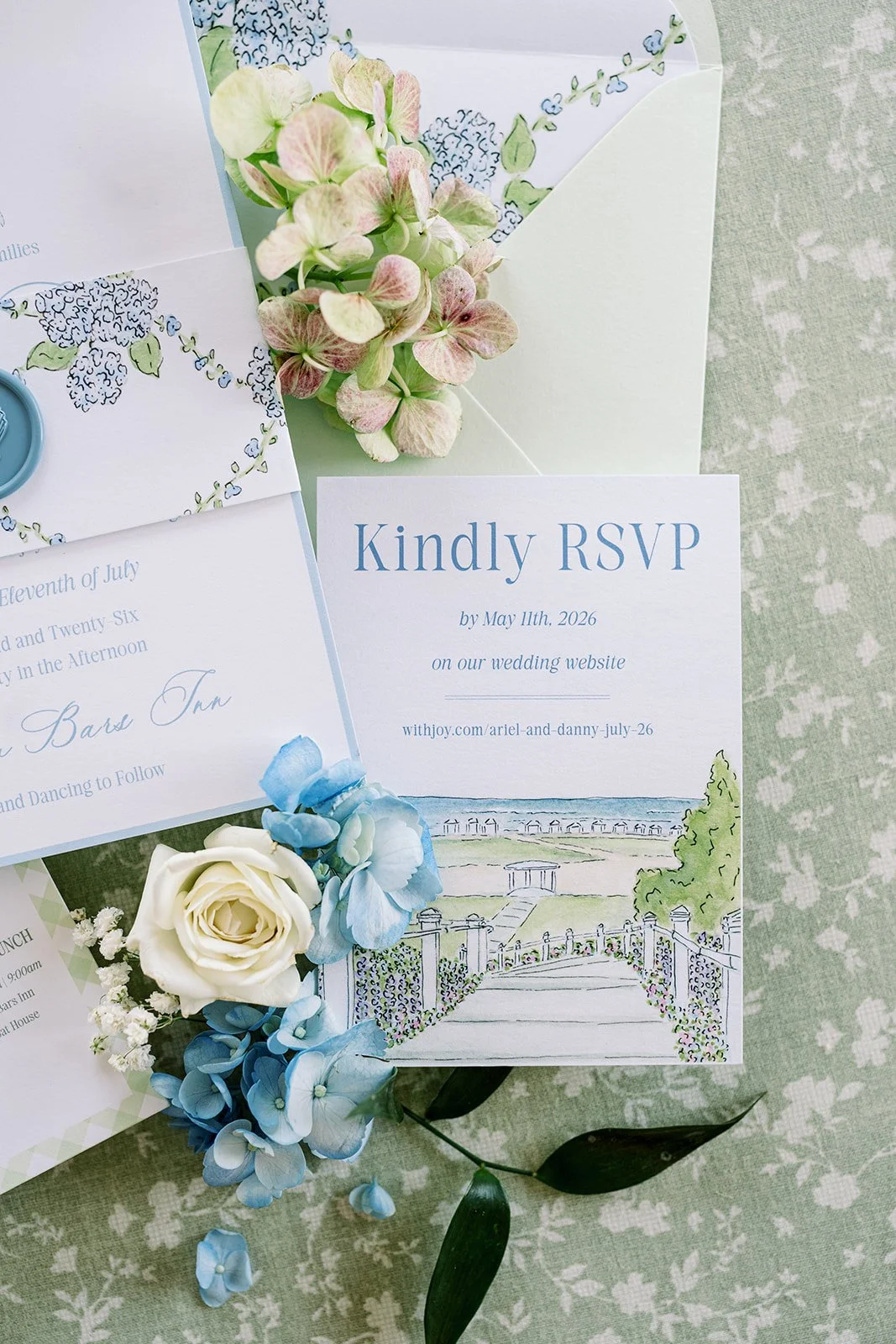 Custom watercolor artwork on RSVP card with various other blue and green wedding stationery with a green background