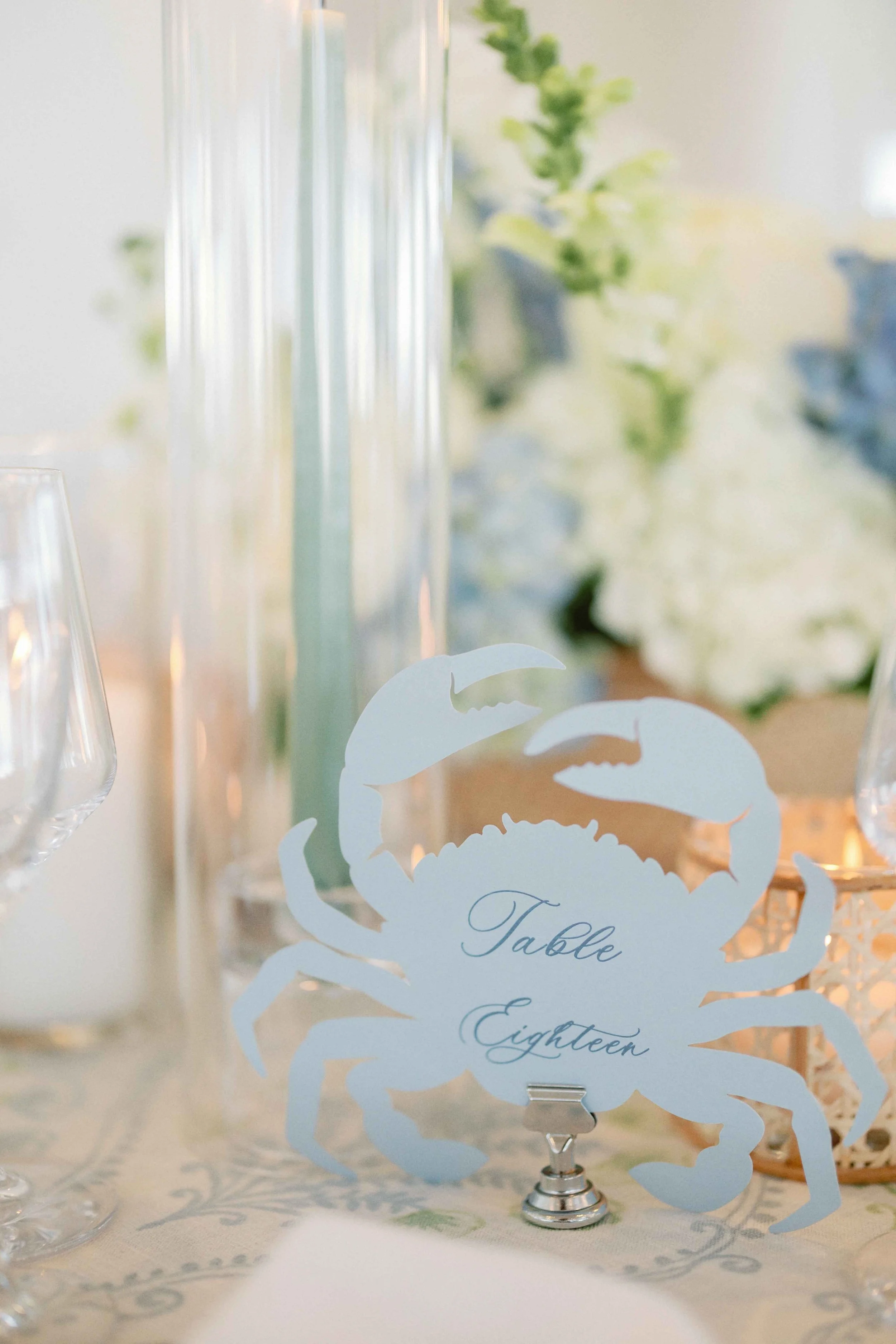 Crab-shaped table number cut-out featuring a table number on it with candles and florals surrounding it