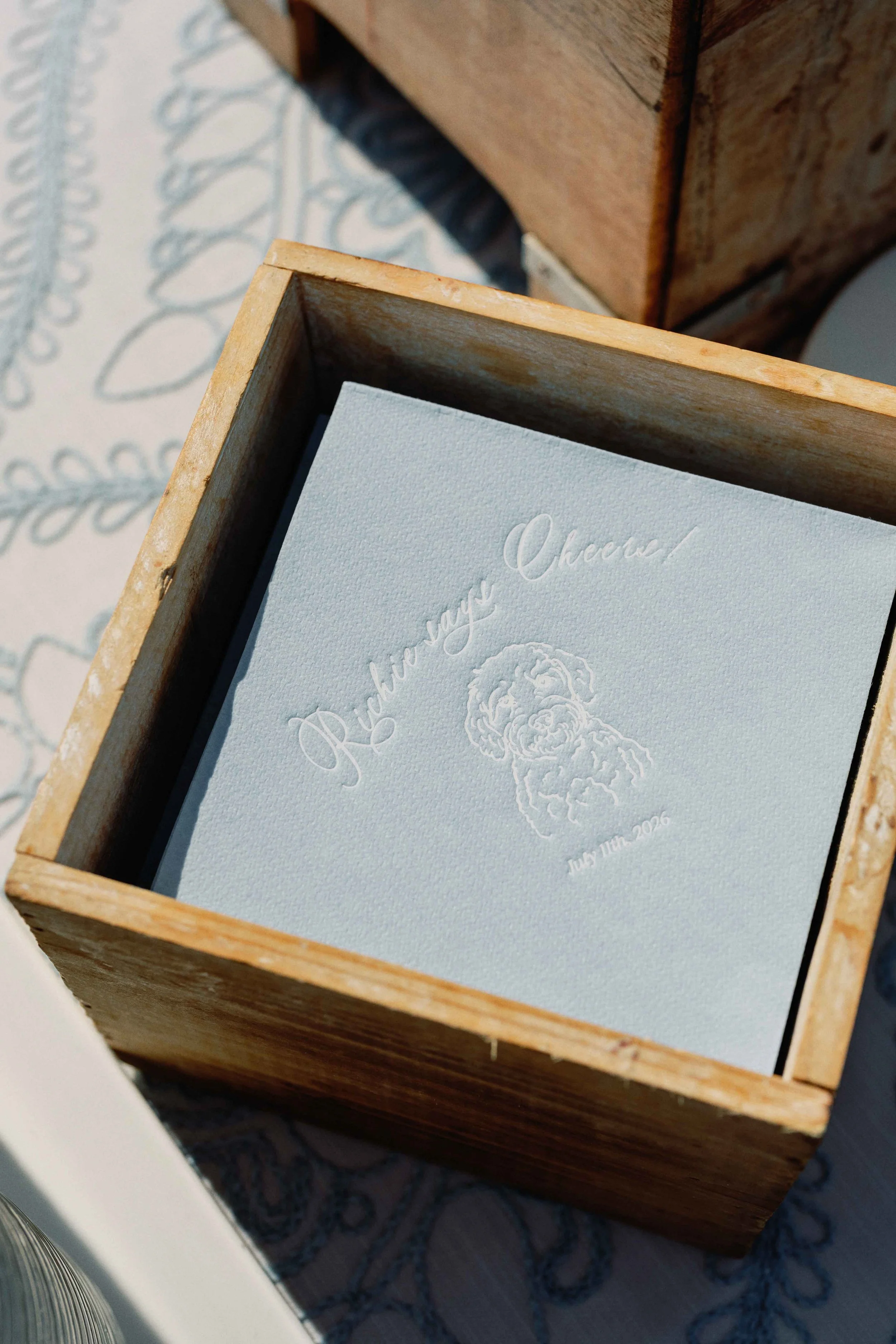 Wooden box on top of a blue and green table cloth holding custom blue napkins for their wedding day