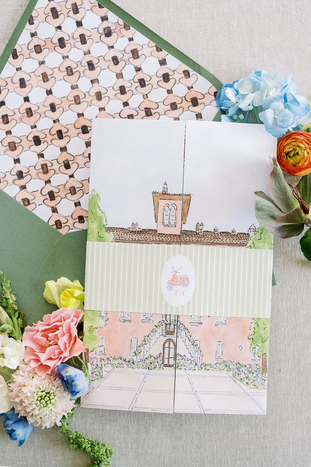 Tri-fold wedding invitation with a watercolor illustration of a wedding venue, envelope, and florals
