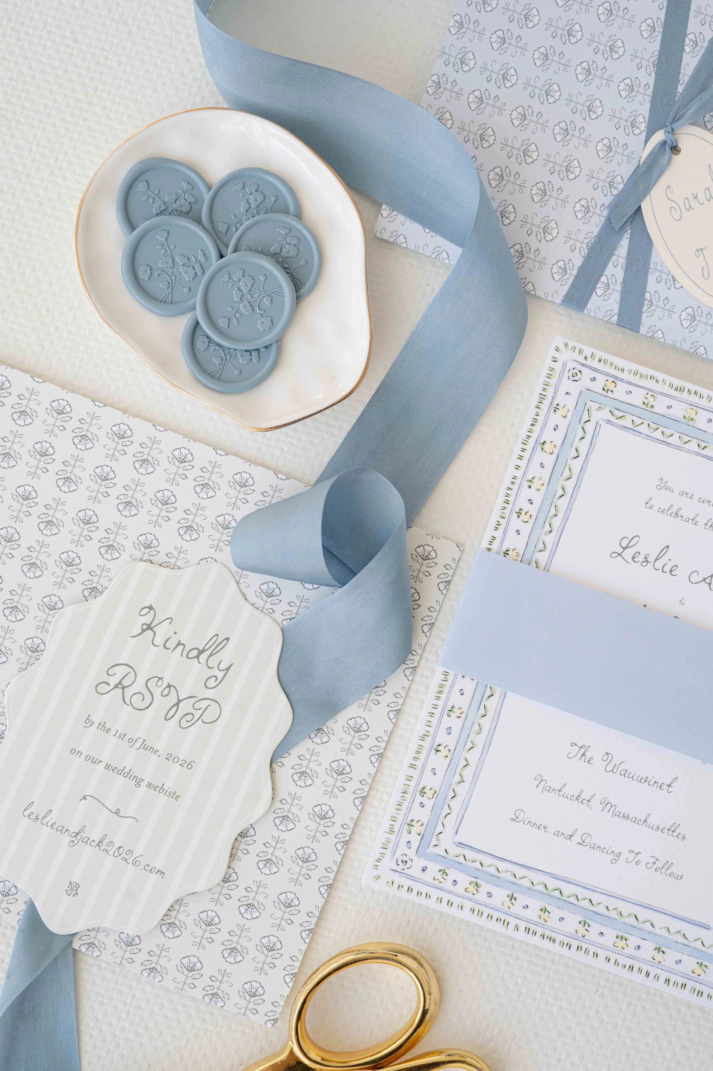 Wedding invitation details with light blue ribbons, wax seals featuring a floral design, and RSVP and event details on decorative paper.