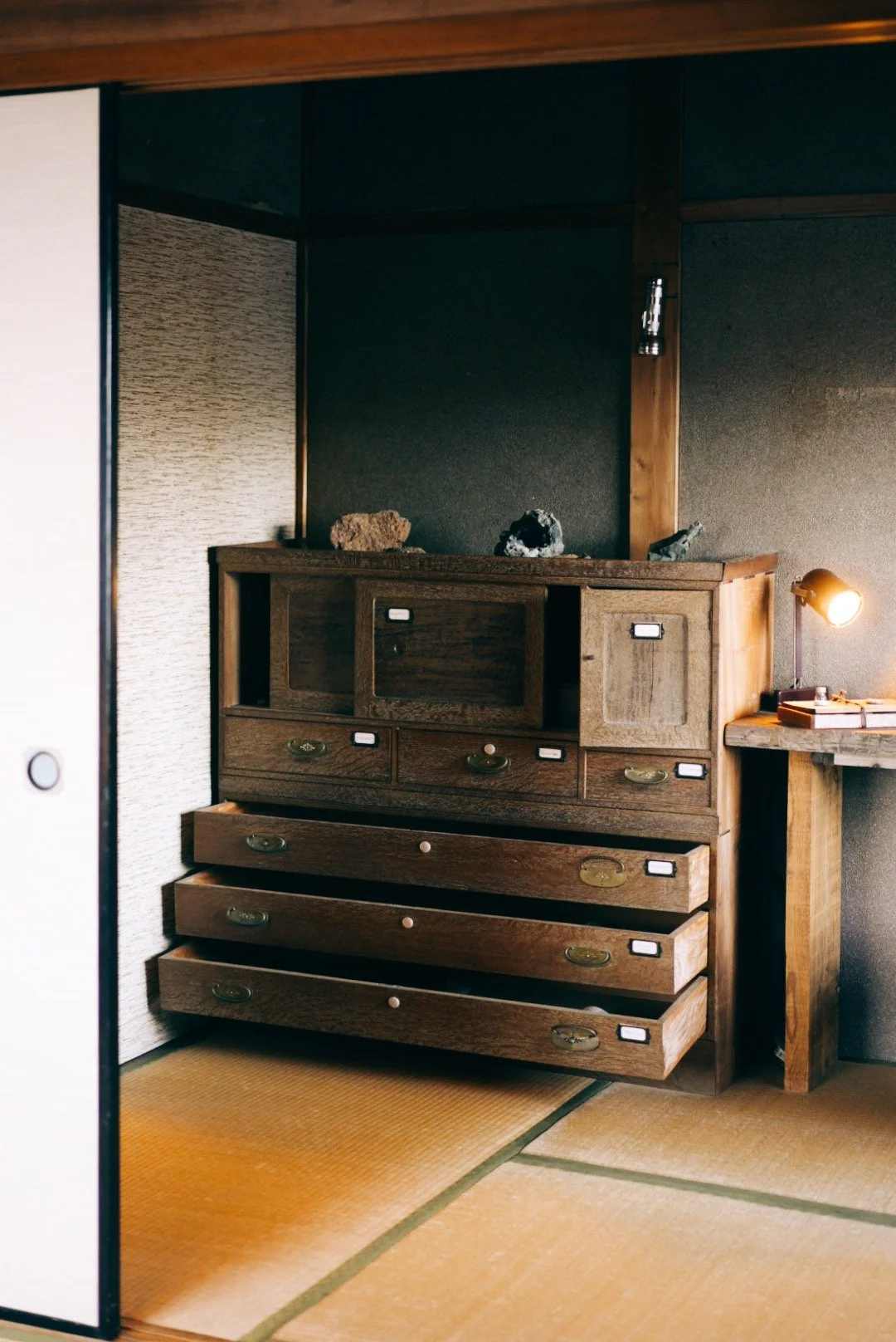 A wooden dresser with multiple drawers inside a traditional Japanese-style room with tatami mat flooring. inside kamikura.hideaway 神倉書斎 in Shingu, Wakayama, Japan. After finishing the kumano kodo.  interior/ Airbnb photography. wabi-sabi.