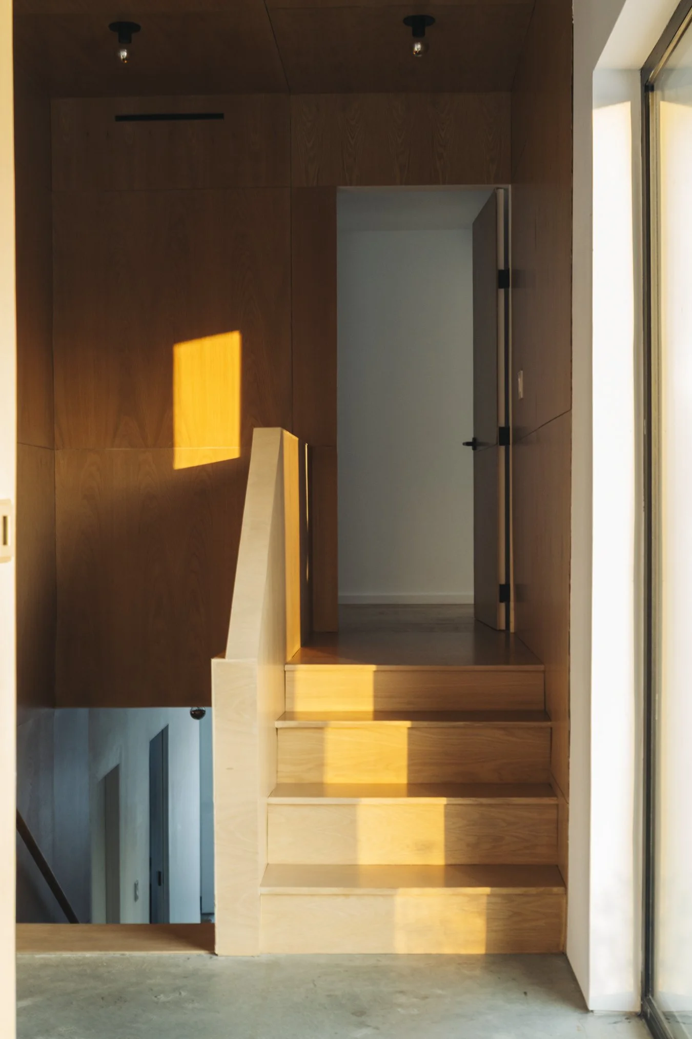 Wooden staircase leading to a doorway, with sunlight casting a yellow square shadow on the wall and stairs. at the Taghkanic house. @redcottageincs. Interior, Airbnb photography.