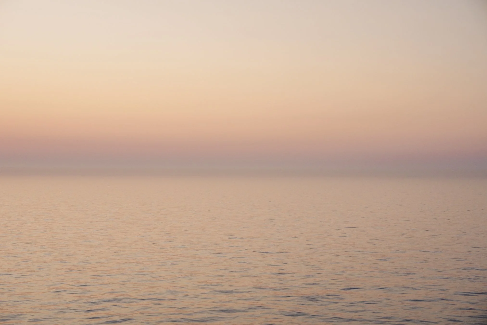 A calm ocean during sunset with pastel pink and orange sky reflected on the water. Oceania Cruise