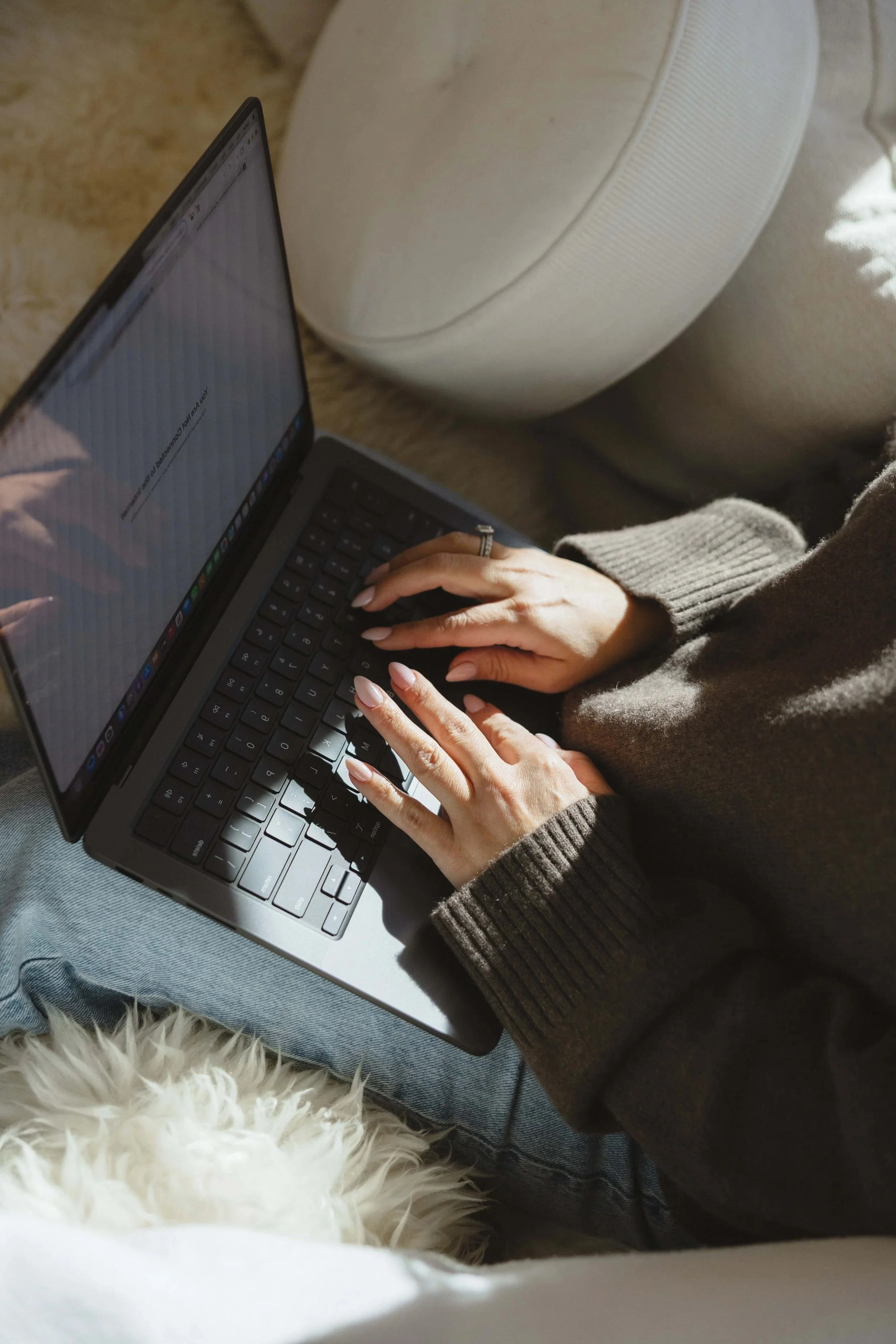 Person using a laptop on their lap, sitting on a couch with sunlight coming in.
