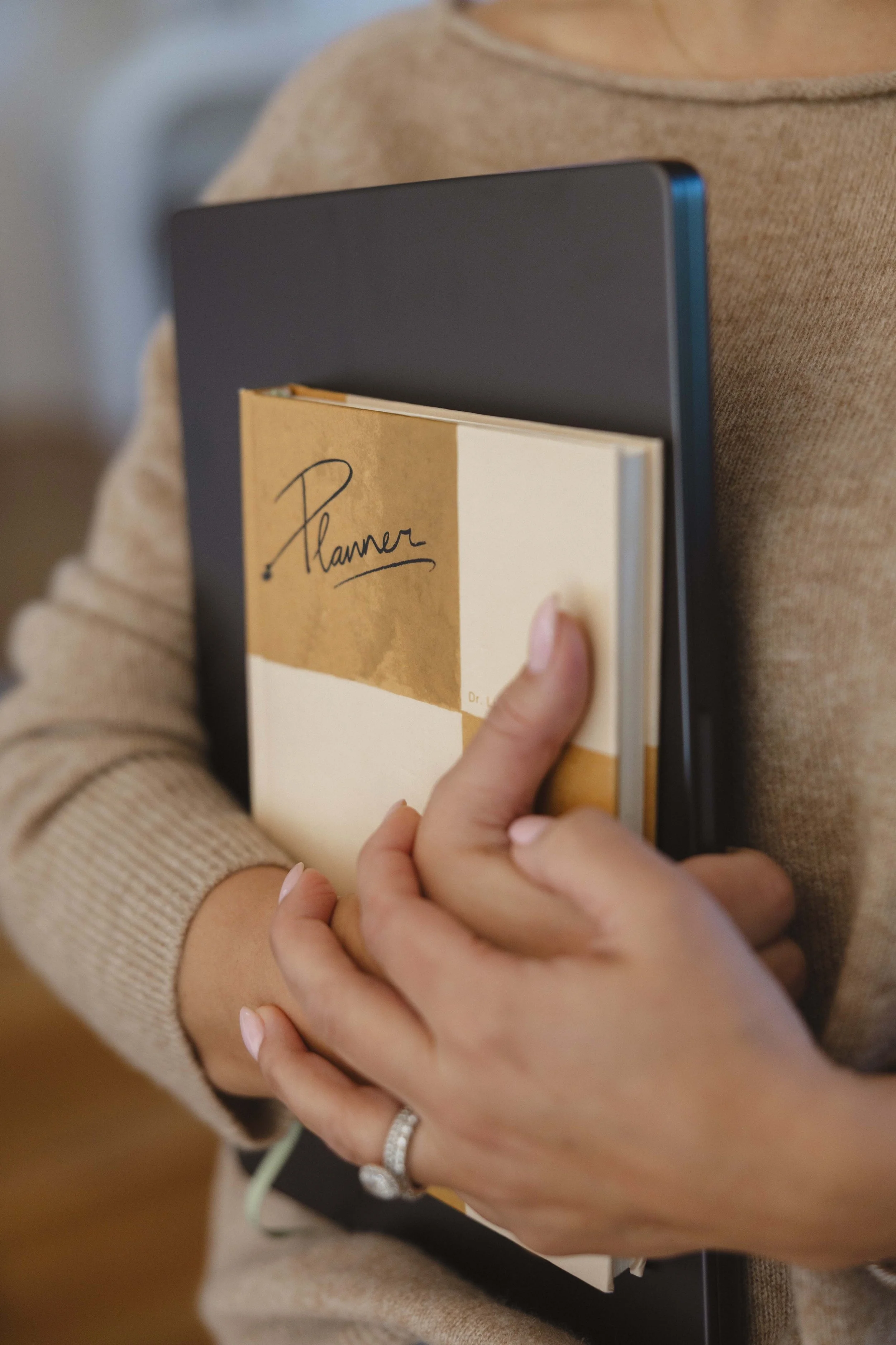 A person holding a planner, a notebook, and a laptop close to their chest.