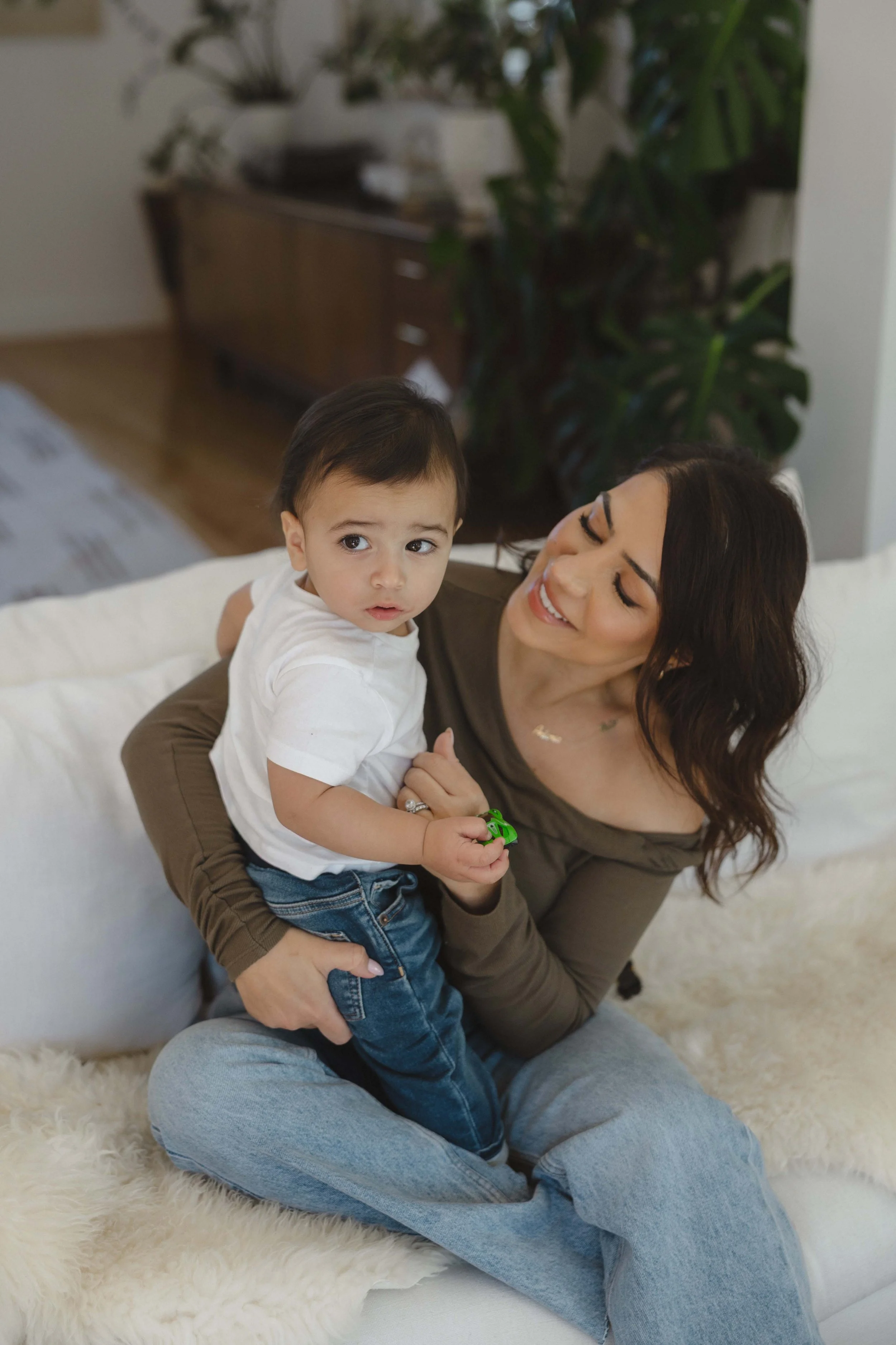 A woman holding a young boy on a white couch in a cozy living room.