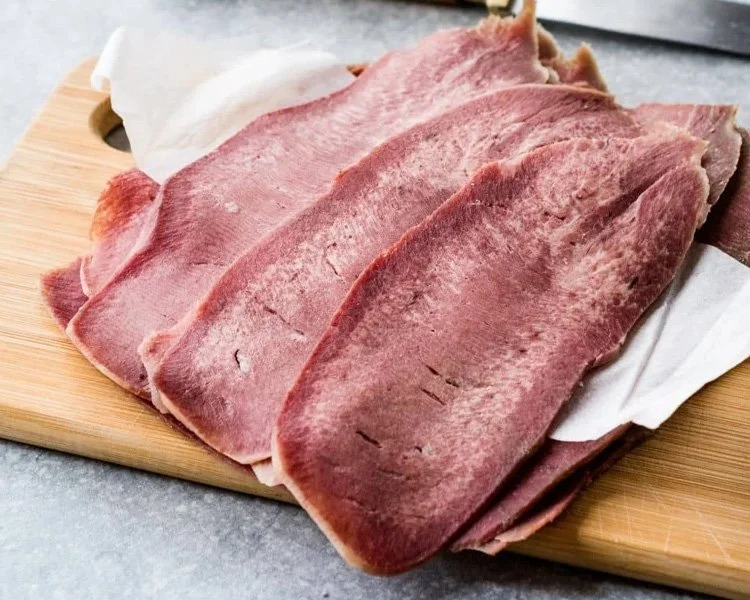 Thin slices of raw ham on a wooden cutting board with paper towel.