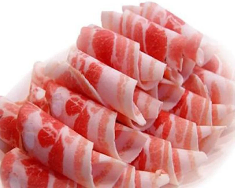Slices of raw bacon rolled up on a white surface.