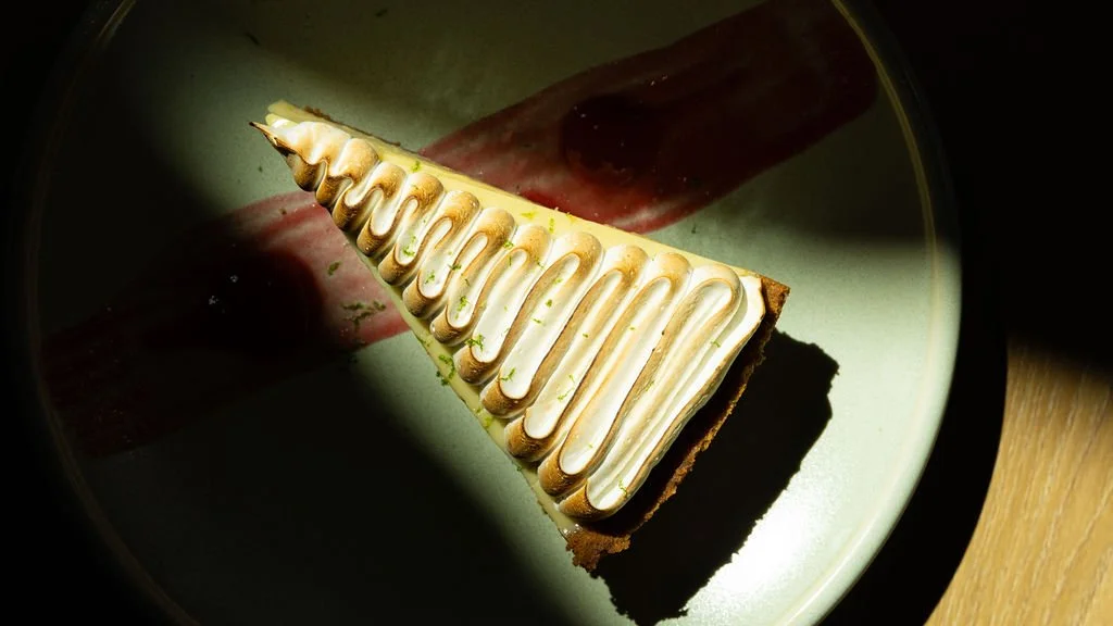A slice of cheesecake with white icing and caramel drizzled on top, on a green plate.