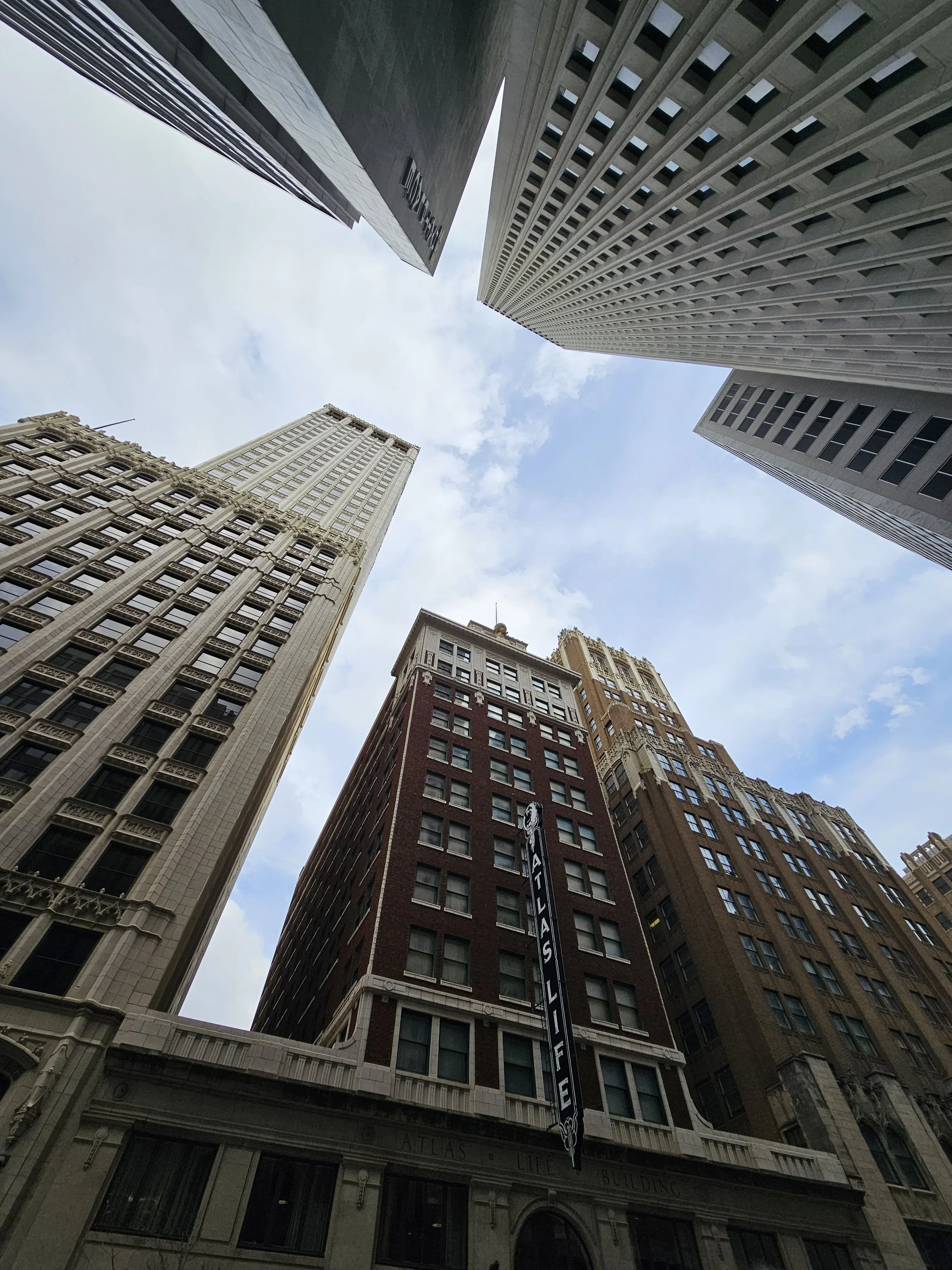 Looking up at tall skyscrapers in downtown, with a cloudy sky overhead."