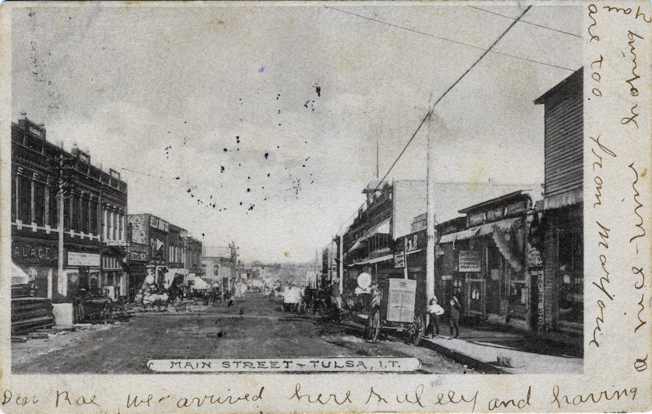 Historical black and white photograph of Main Street in Tulsa, Oklahoma, showing early 20th century storefronts, pedestrians, and horse-drawn carriages along a dirt road.