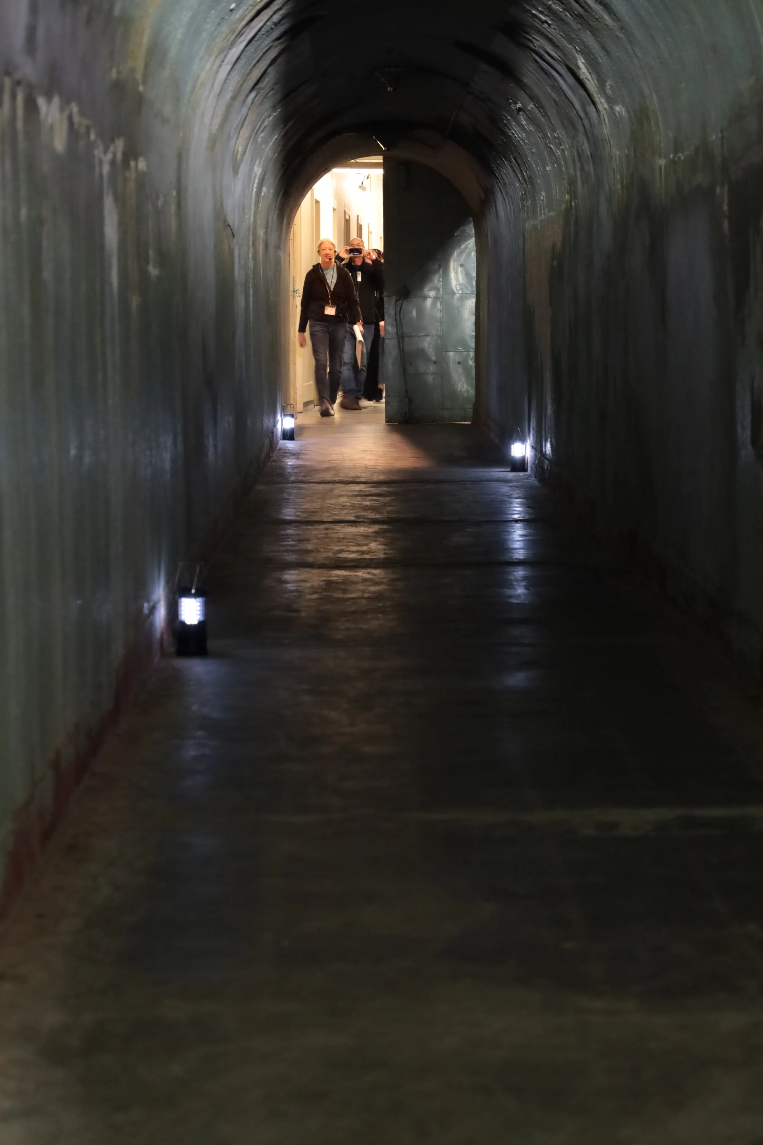 People walking through a dimly lit, enclosed tunnel with small lights on the floor along the sides.
