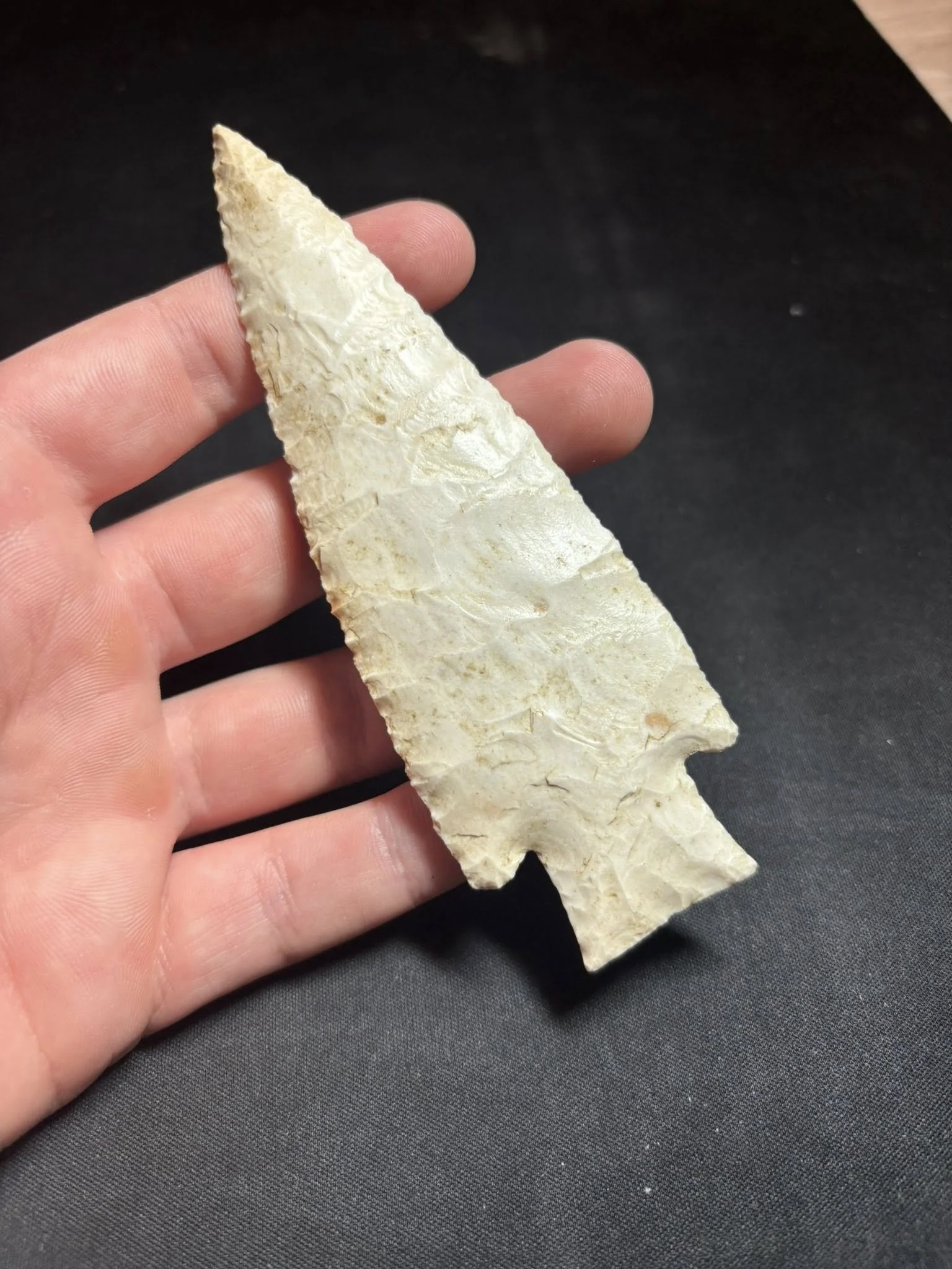 A person holding a white, leaf-shaped arrowhead made of stone against a black background.