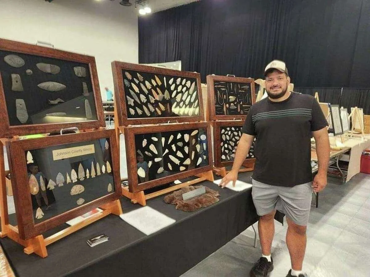 Man standing next to framed artwork with abstract patterns on display at an indoors event.